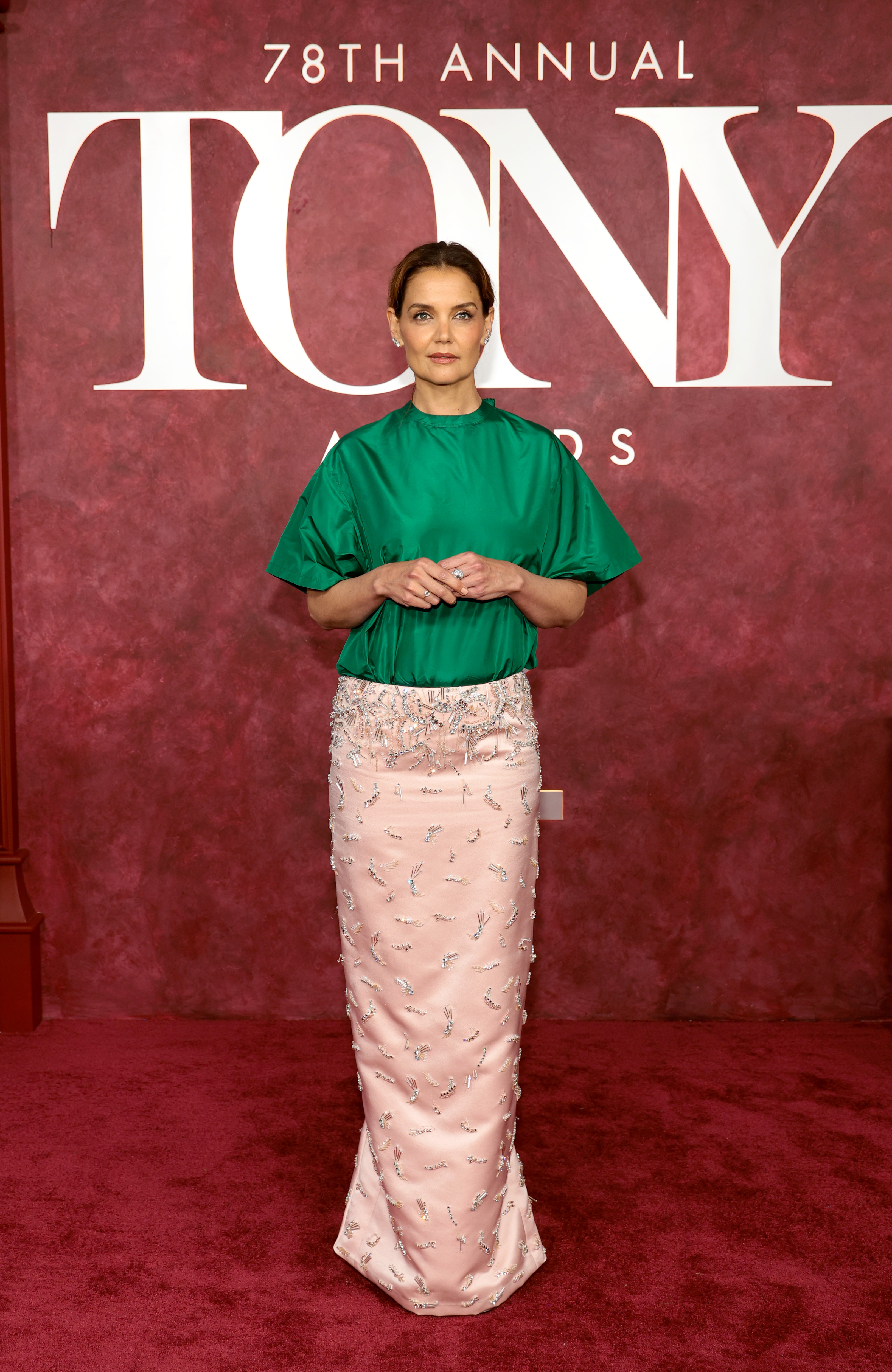 Enmarcada por las letras oficiales de los Premios Tony, Katie Holmes adopta una postura amplia con las manos suavemente entrelazadas. La composición de pies a cabeza resalta el equilibrio poco convencional de la prenda entre volumen, brillo y detalles ornamentales.