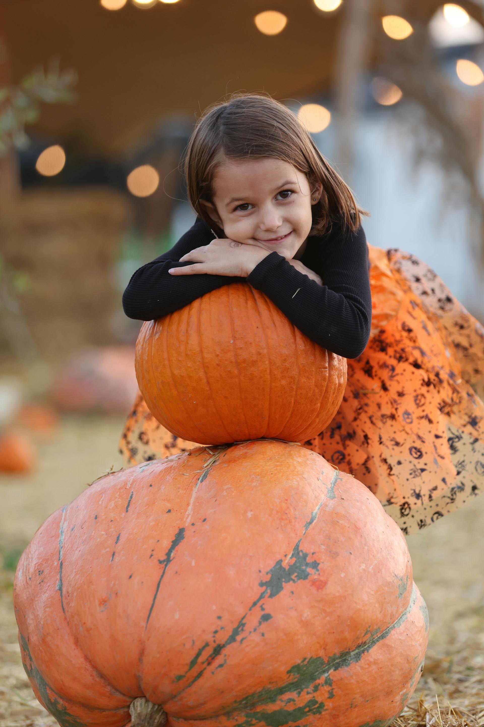 Una niña apoyando la cabeza sobre una pila de calabazas | Fuente: Pexels