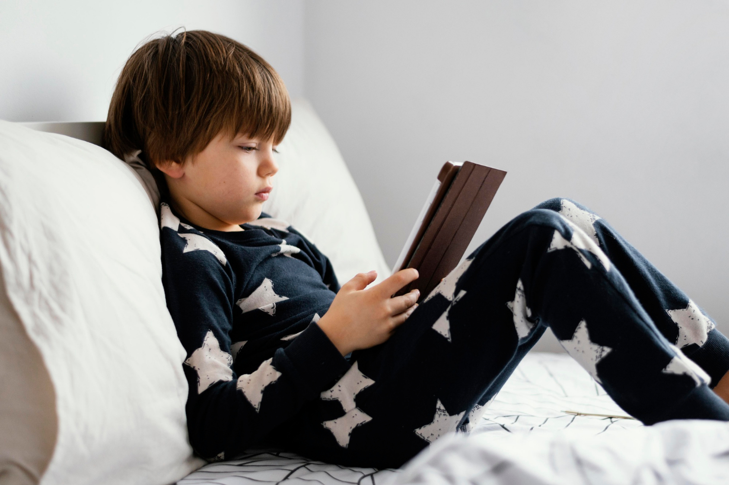 Un niño sentado en la cama con su tableta digital | Fuente: Freepik