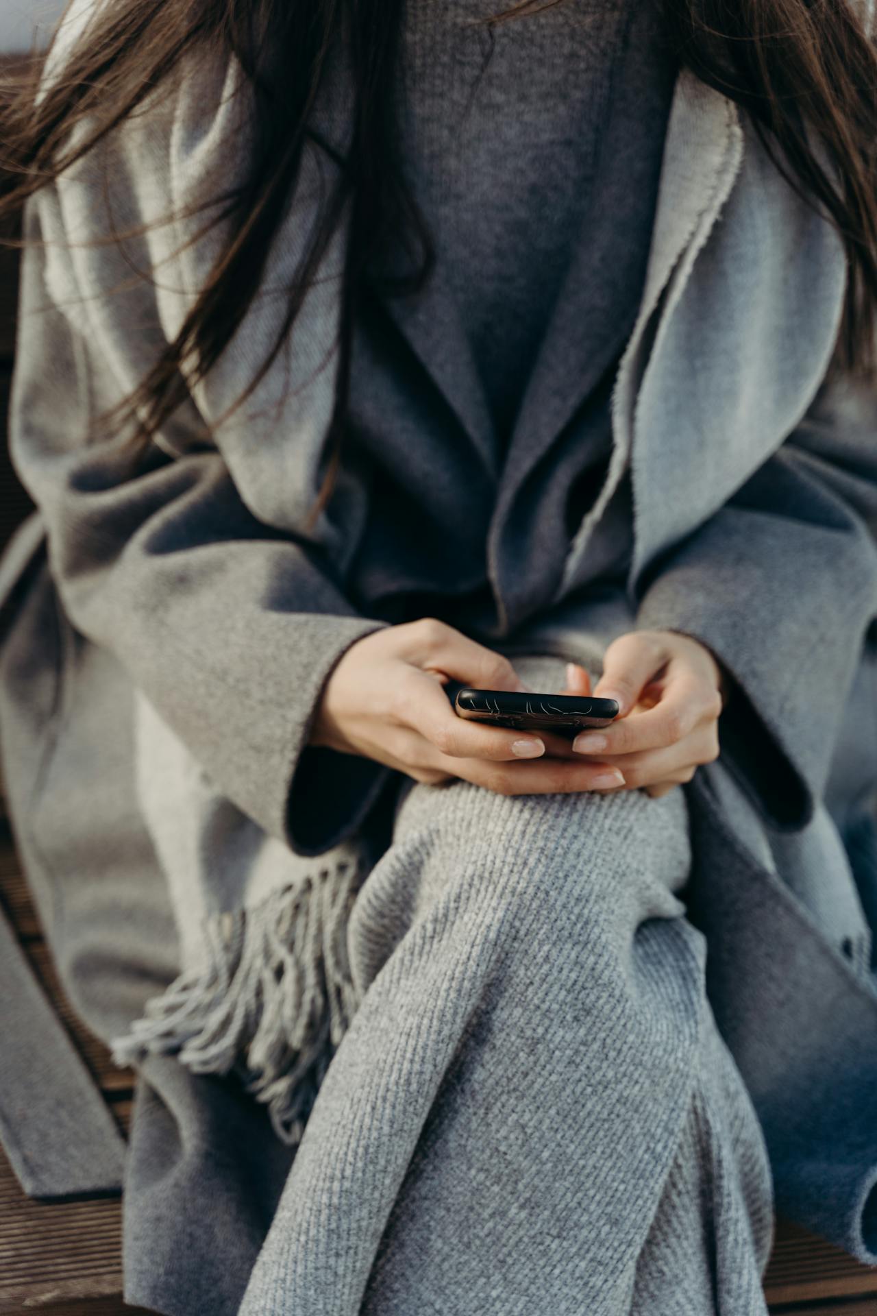 Una mujer con chaqueta gris sujetando su teléfono | Fuente: Pexels