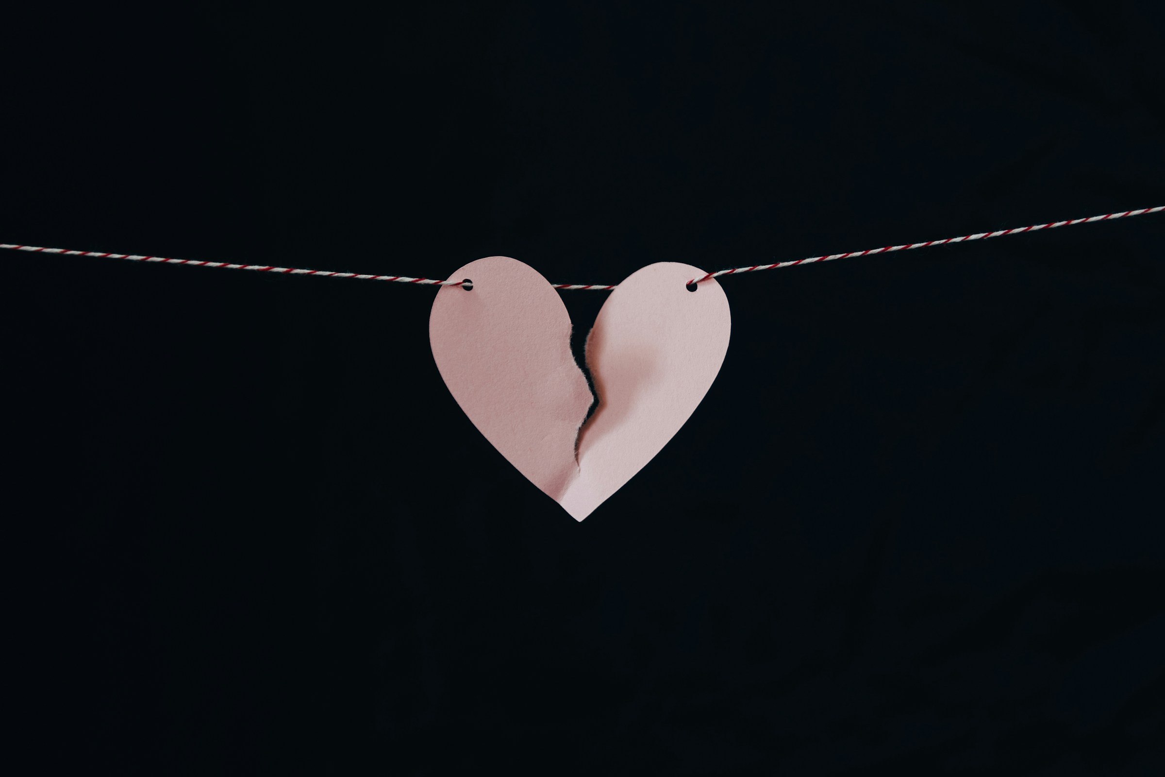 Un corazón de papel rosa roto colgando de un alambre | Fuente: Unsplash