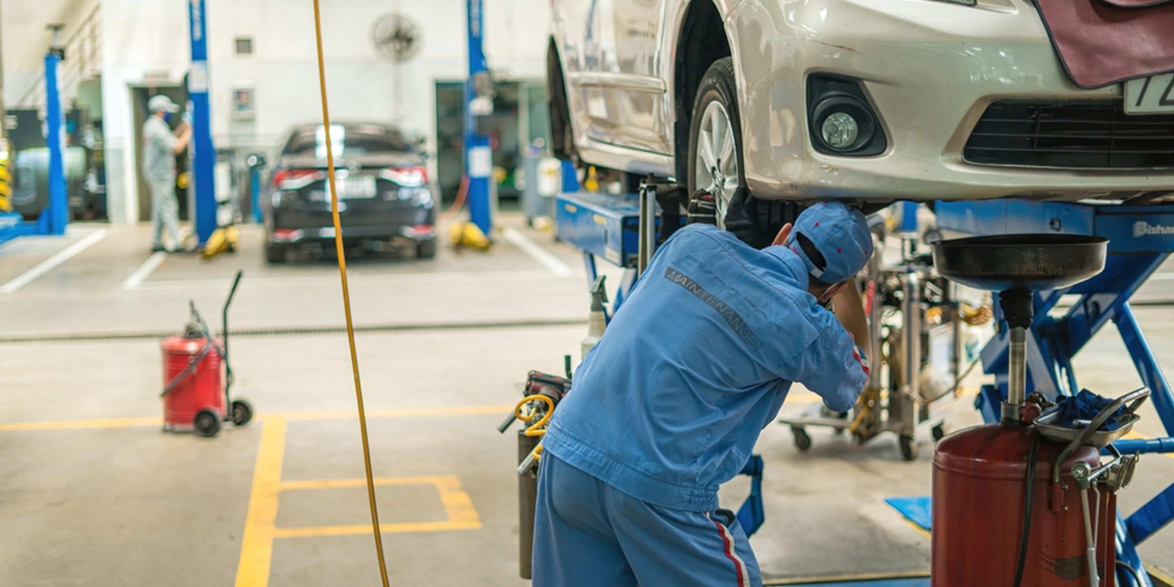 Un mecánico trabaja debajo de un auto levantado en un ajetreado taller de reparación de automóviles | Fuente: Shutterstock
