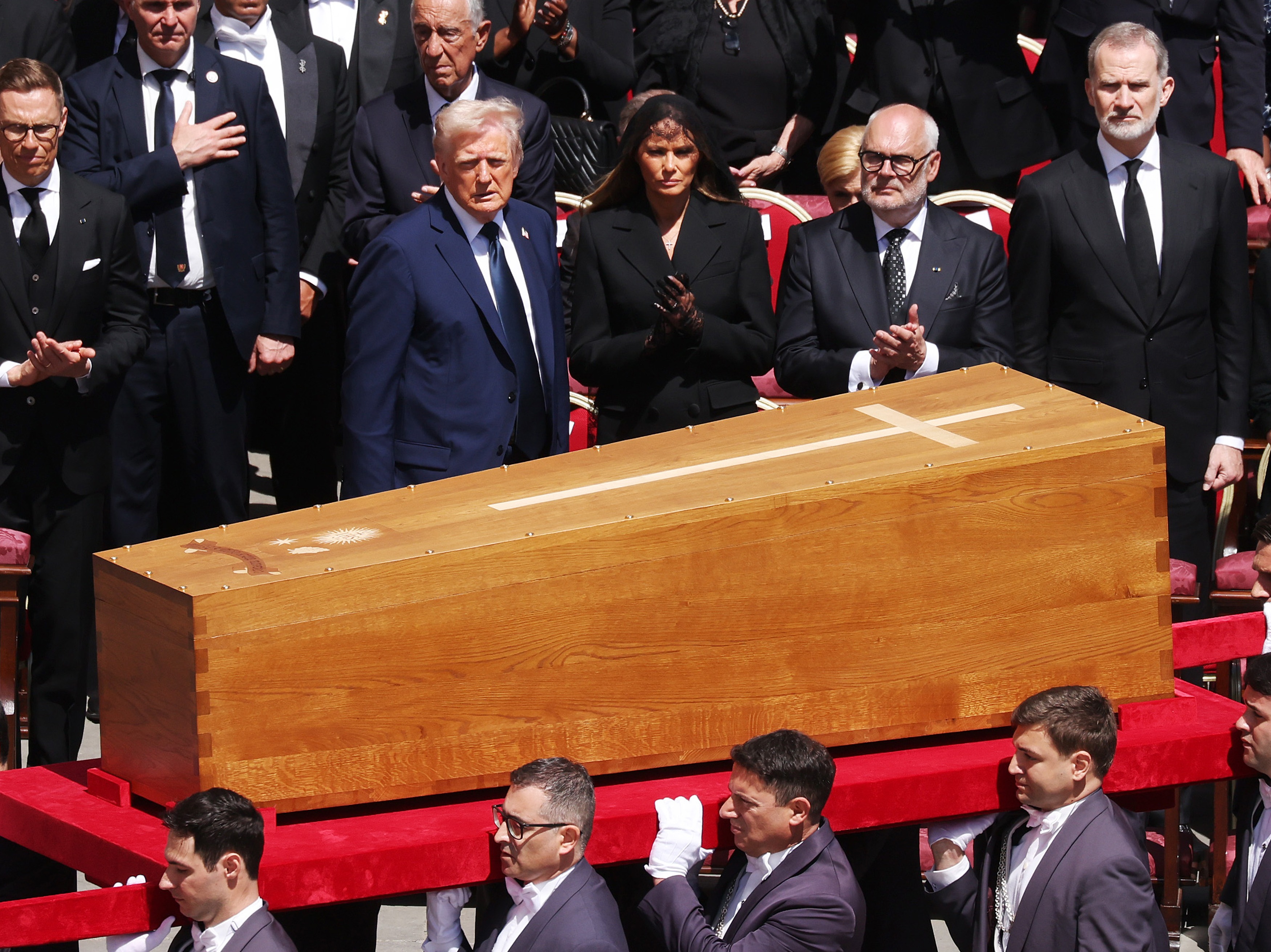 Líderes mundiales, junto a Donald y Melania, observan cómo el féretro del papa Francisco sale lentamente de la Plaza de San Pedro. Algunos aplauden en homenaje, otros colocan las manos sobre el corazón, mientras unos pocos permanecen callados y sombríos, presentando sus respetos.