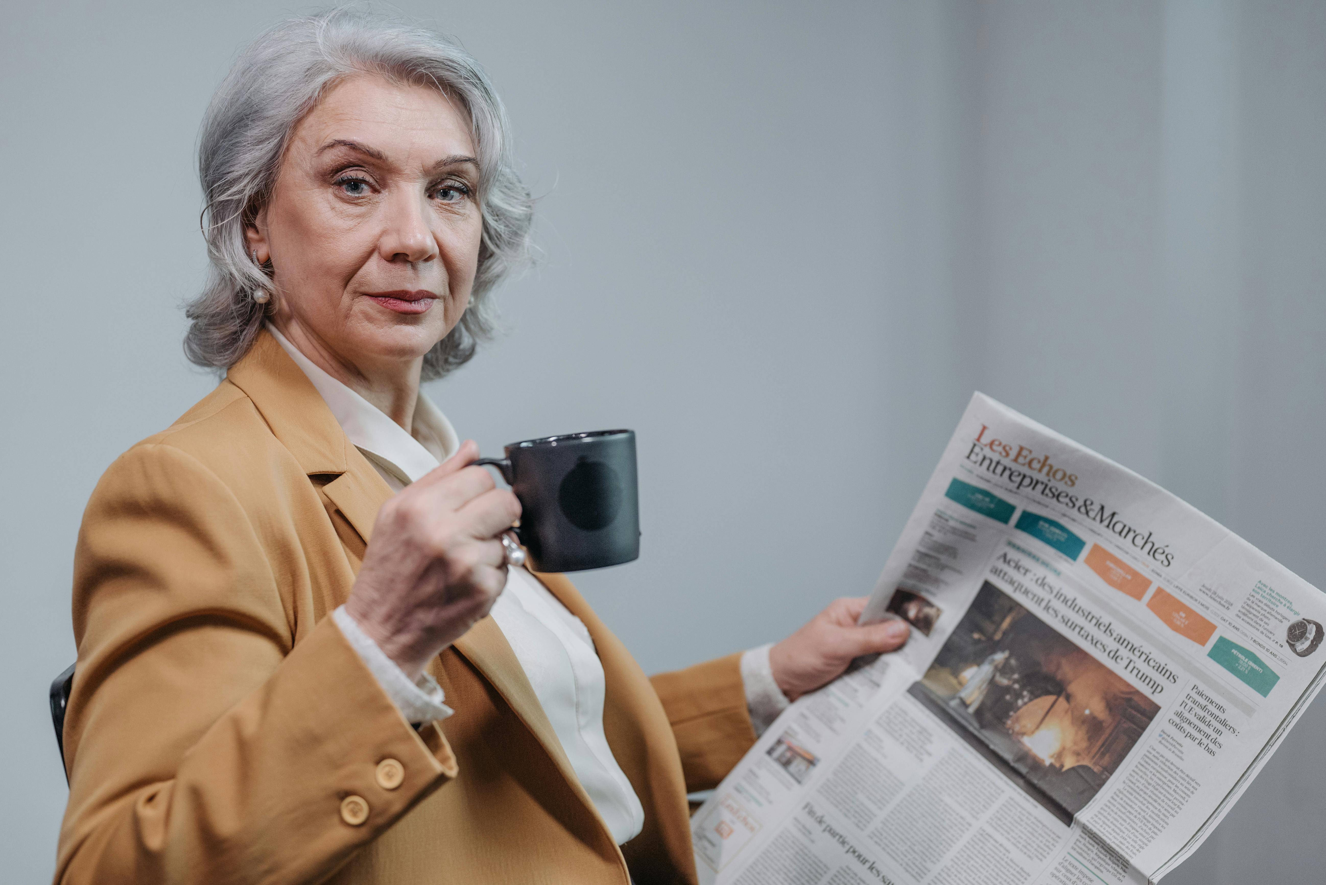 Una mujer seria tomando café y leyendo un periódico | Fuente: Pexels