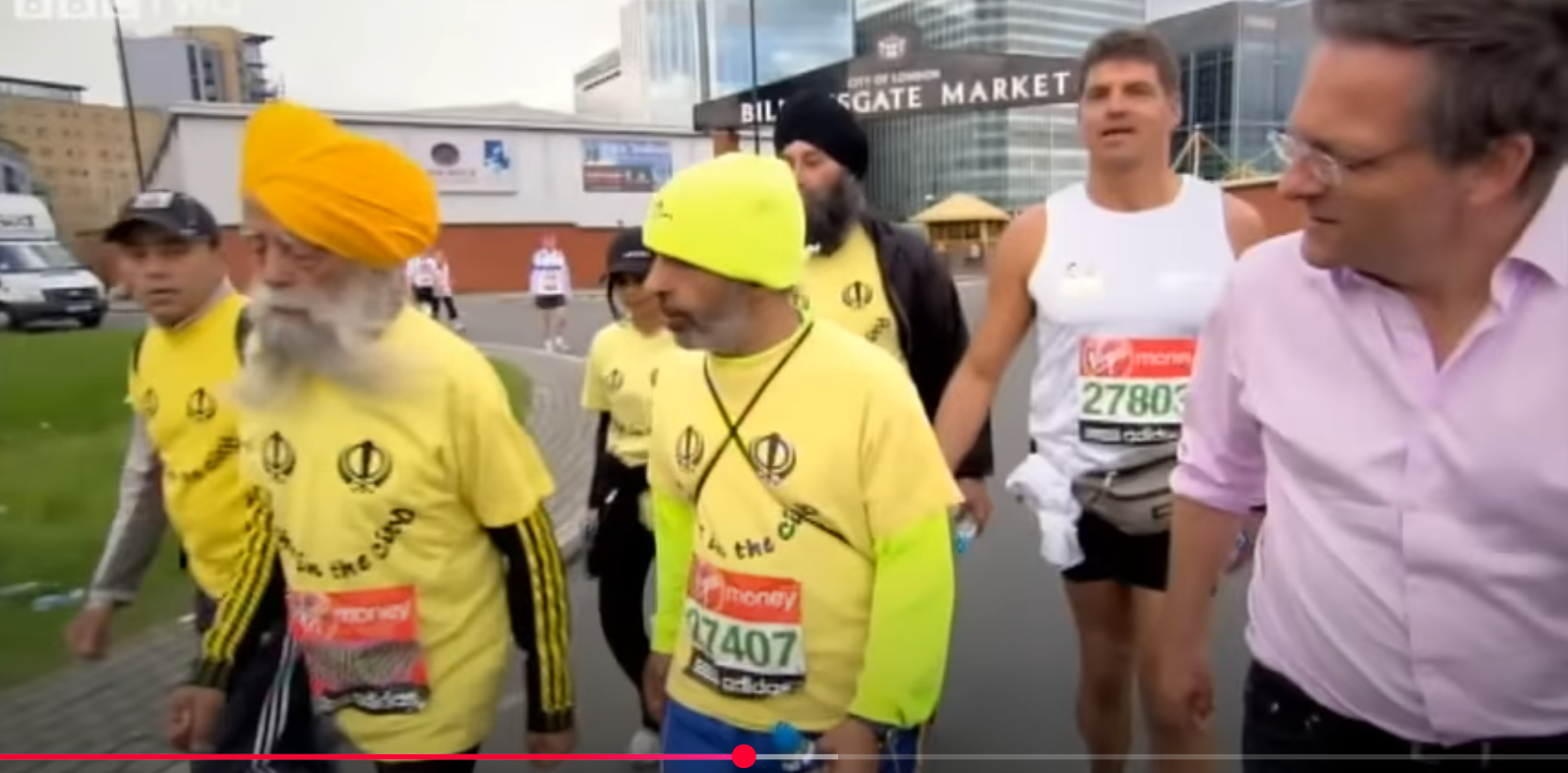 Fauja Singh (segundo por la izquierda) entrevistado por un periodista de la BBC durante el Maratón de Londres. De un vídeo del 6 de agosto de 2012. | Fuente: YouTube/BBC