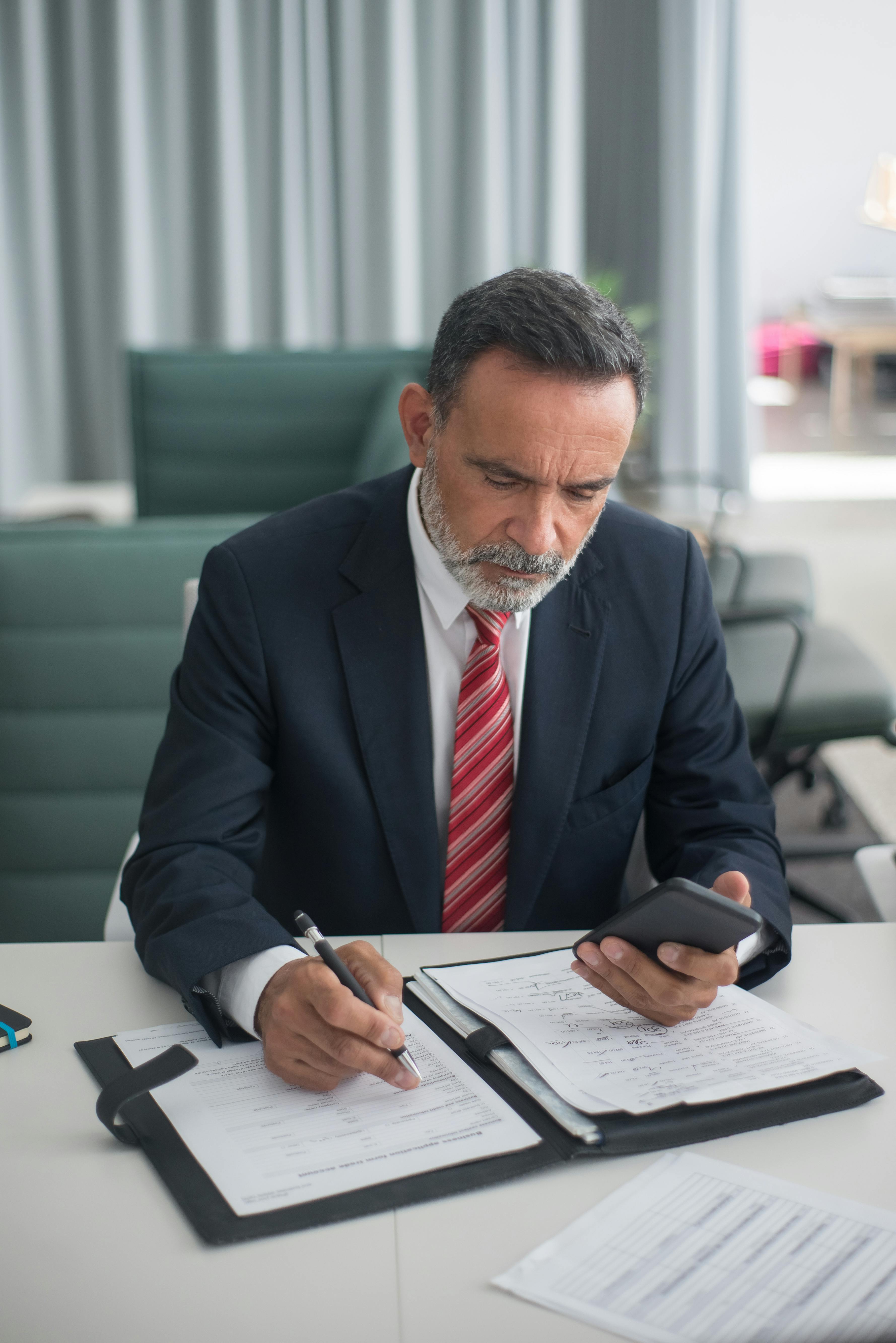 Un hombre sostiene su teléfono mientras escribe algo | Fuente: Pexels