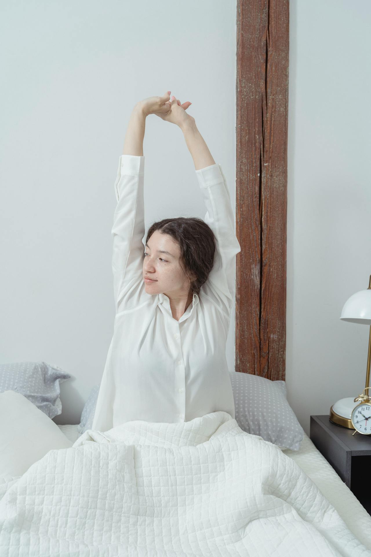 Una mujer estira los brazos sentada en la cama | Fuente: Pexels
