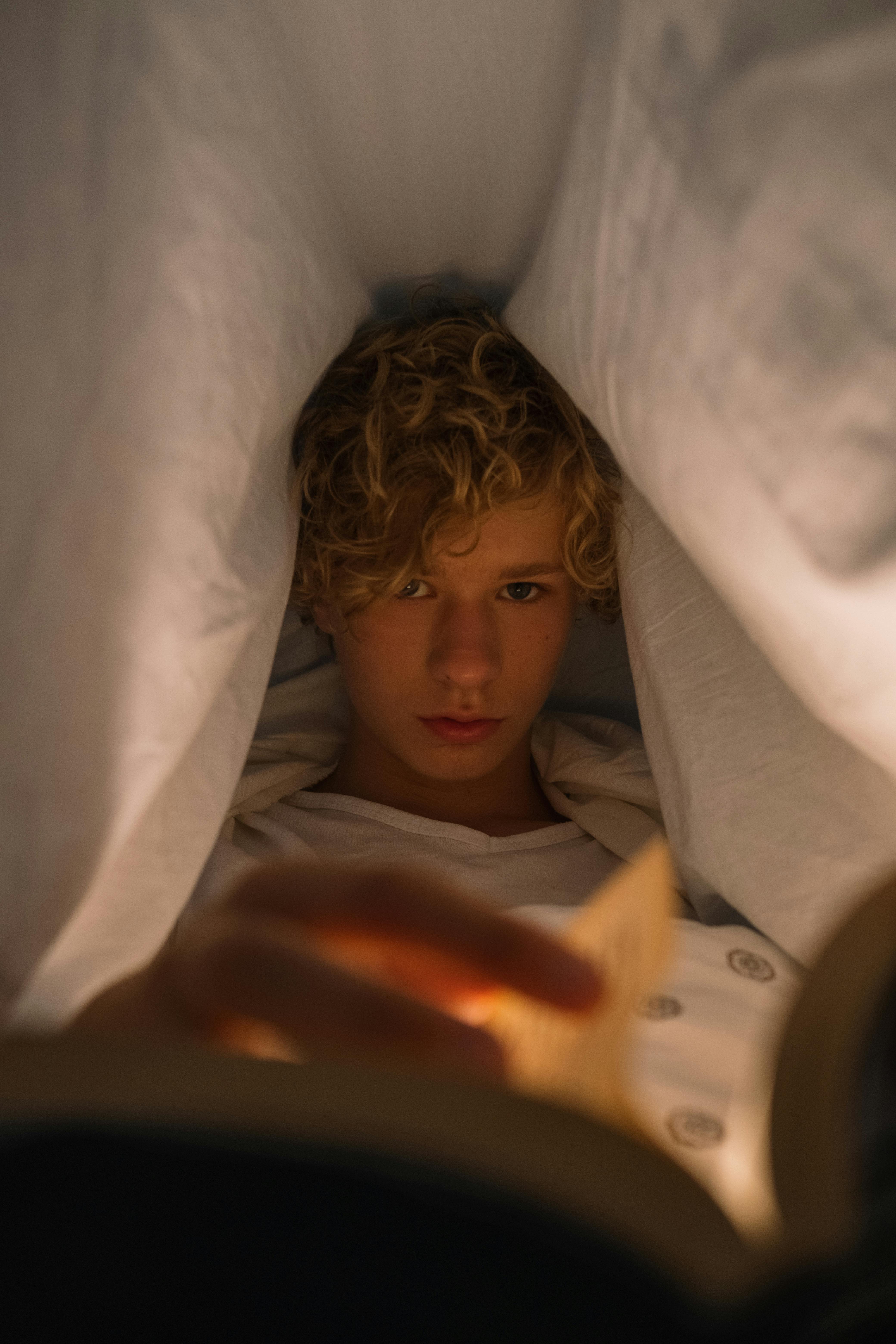 Adolescente leyendo por la noche bajo la sábana | Fuente: Pexels