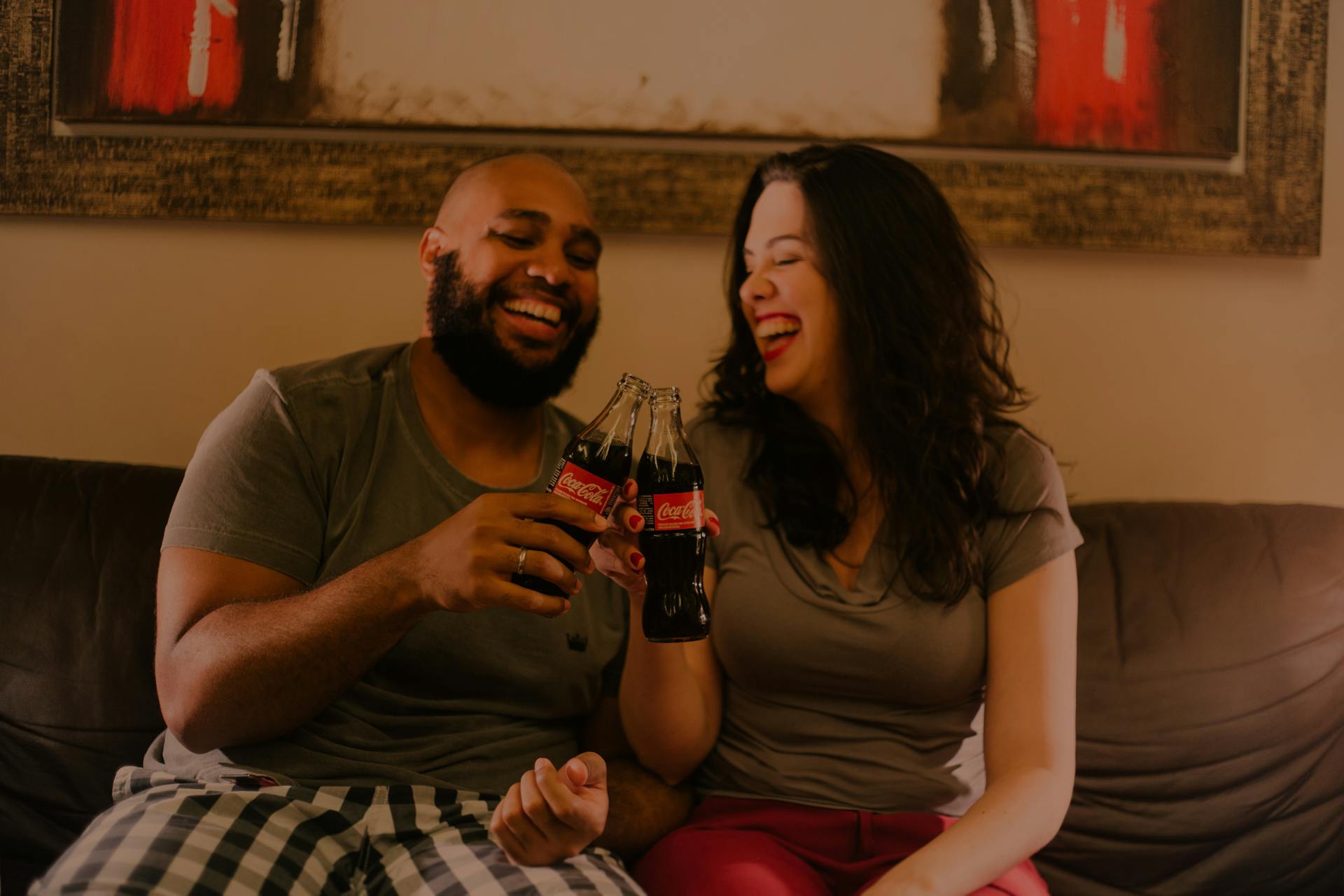 Una pareja ríe mientras sostiene botellas de refresco | Fuente: Pexels