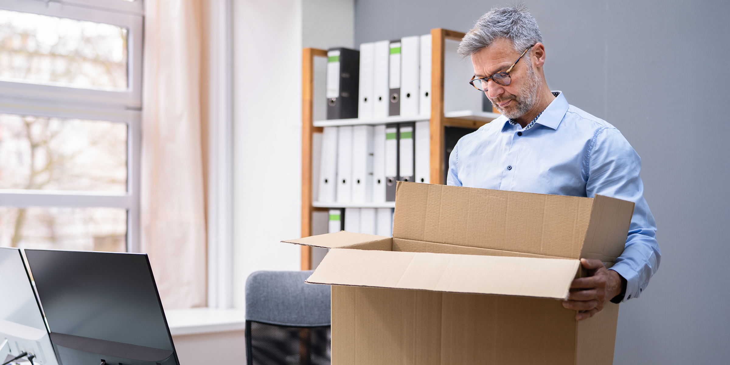 Un hombre de pie en su oficina y mirando una caja de cartón abierta mientras empaqueta sus pertenencias | Fuente: Shutterstock