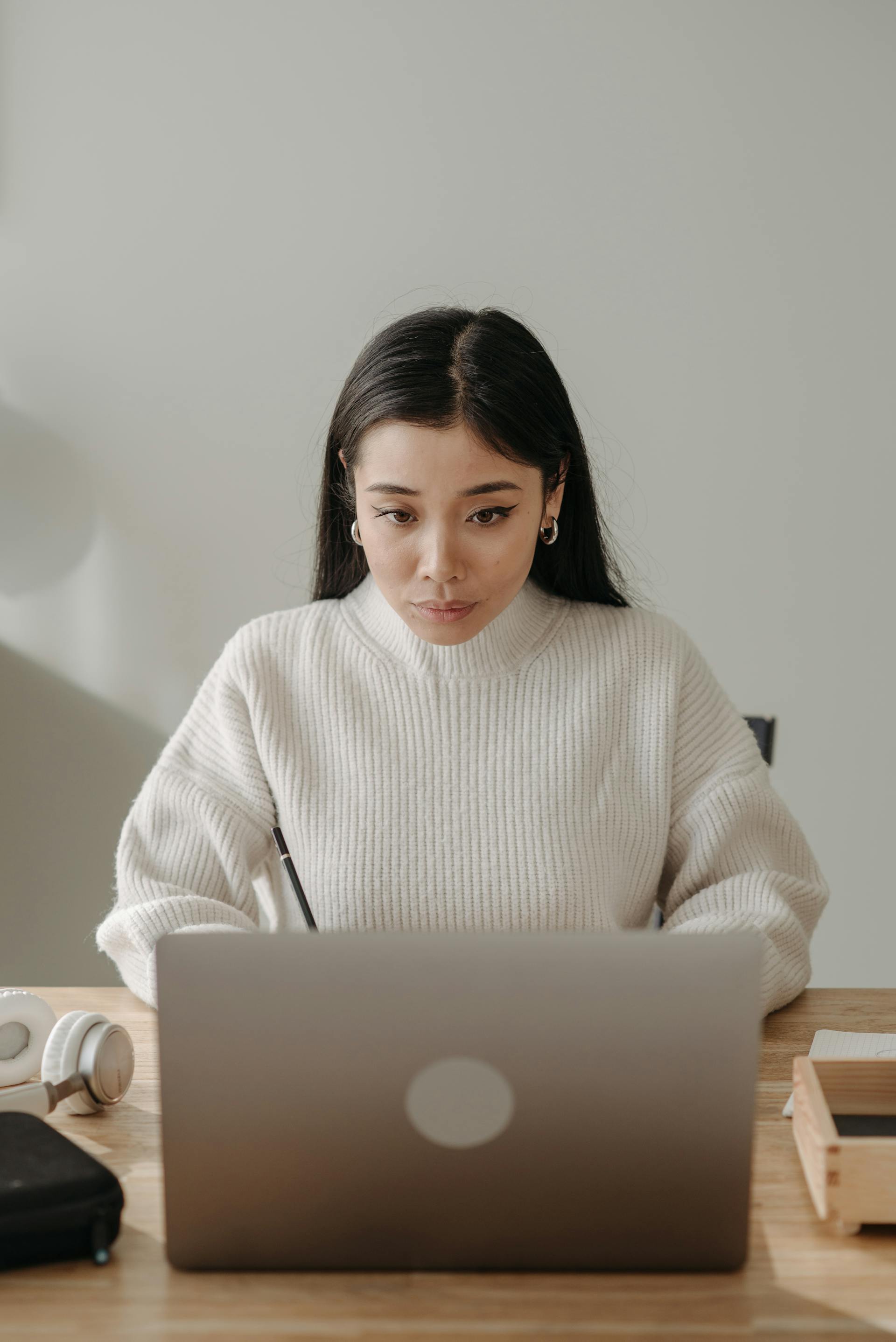 Mujer morena con jersey blanco mirando atentamente un portátil | Fuente: Pexels