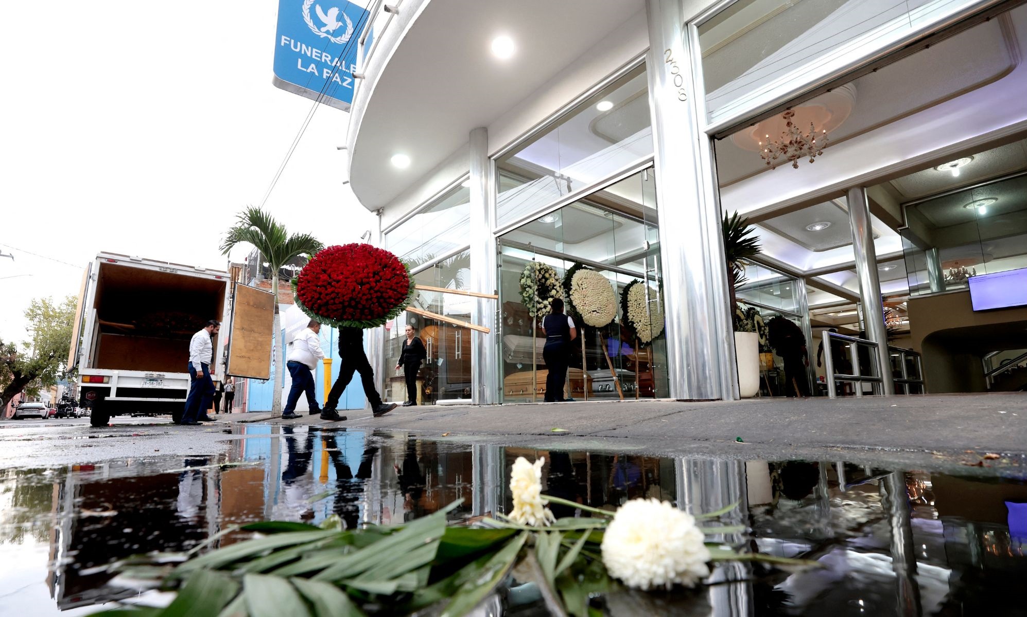 Personas entrando con flores a una funeraria. | Fuente: Getty Images.