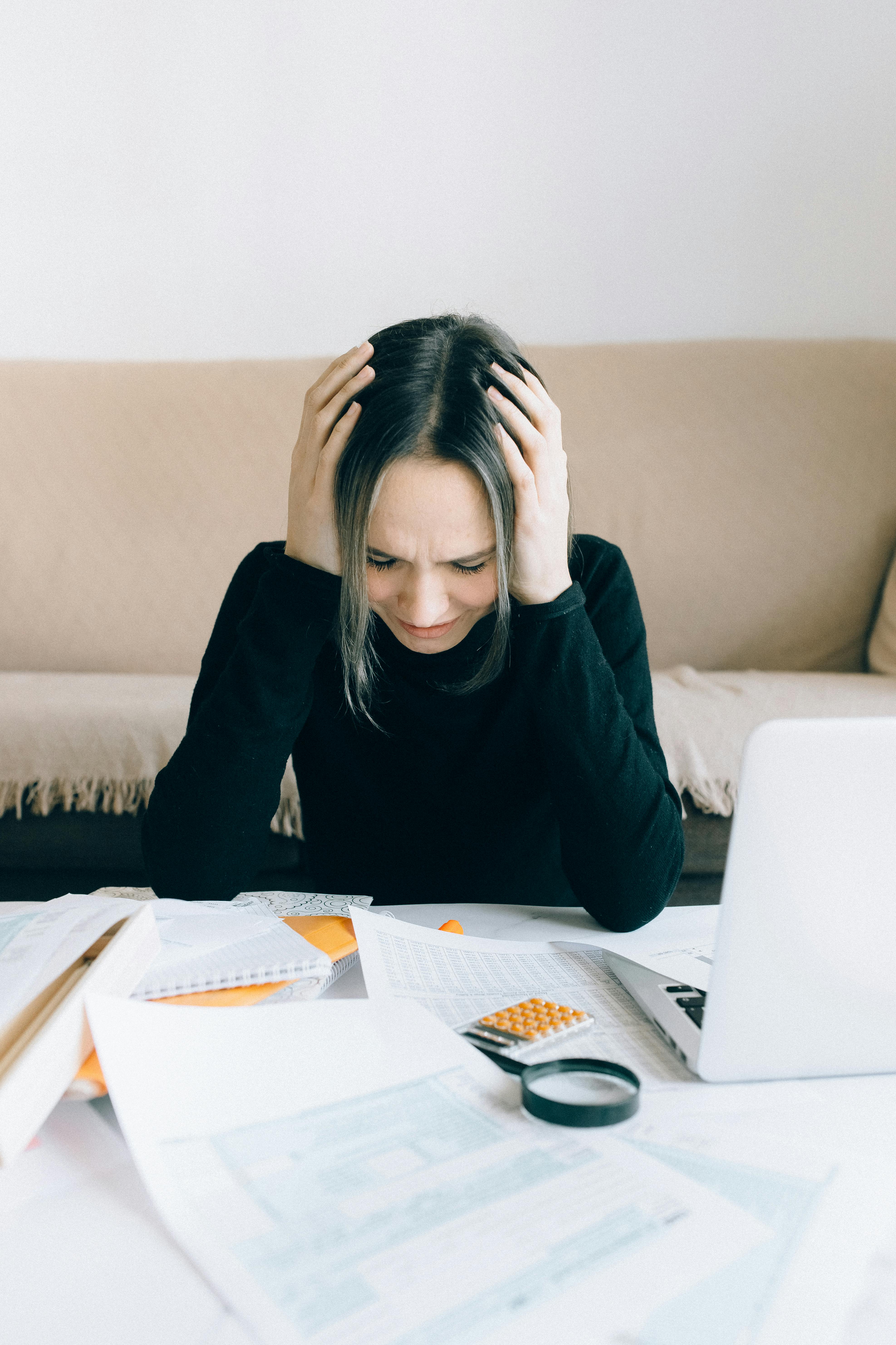 Una mujer sentada en una mesa y sujetándose la cabeza | Fuente: Pexels