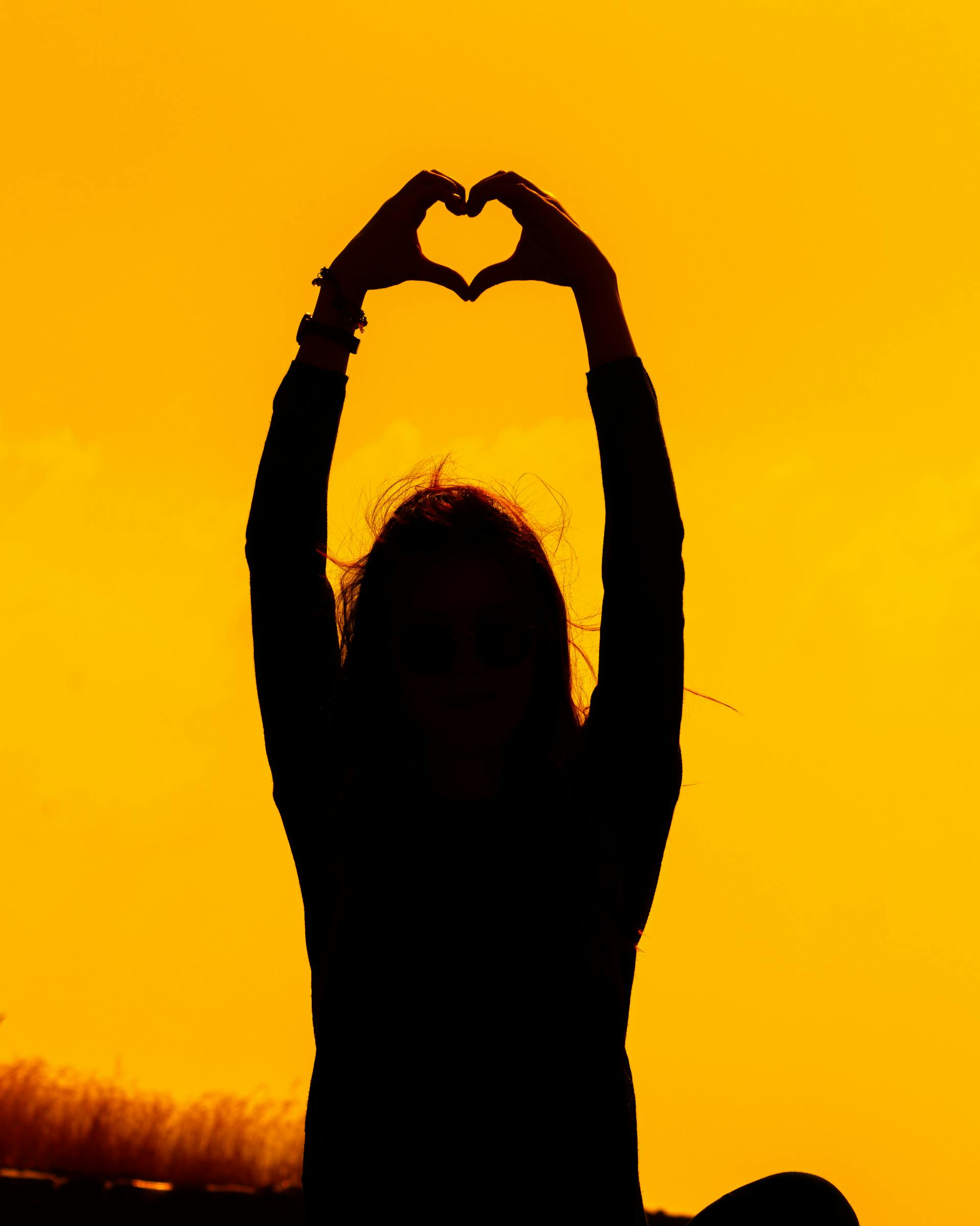 La silueta de una mujer haciendo la forma de un corazón con las manos al atardecer | Fuente: Pexels