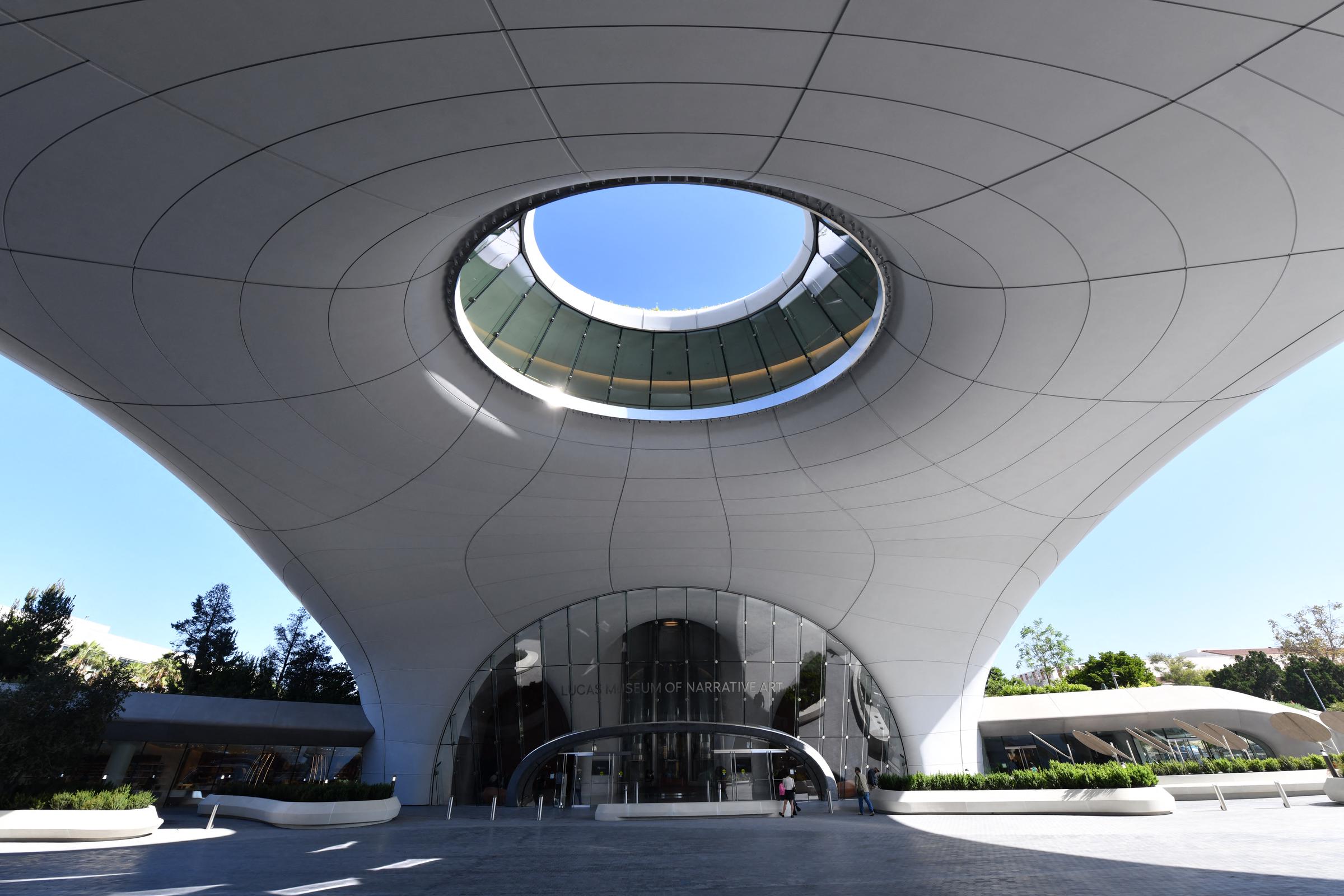 La entrada principal del museo se encuentra bajo la fachada curva del edificio y la gran abertura hacia el cielo. La imagen destaca cómo la arquitectura crea un espacio público protegido bajo la estructura. | Fuente: Getty Images