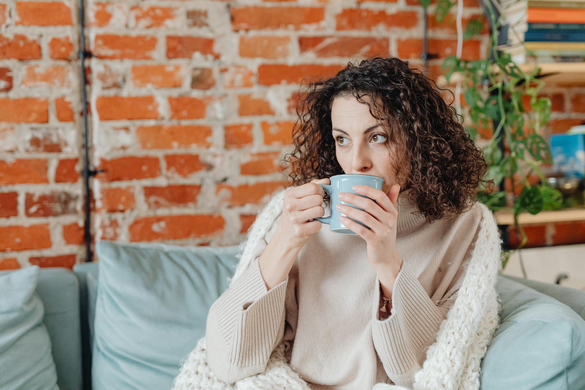 Una mujer tomando una bebida caliente en un sofá | Fuente: Pexels