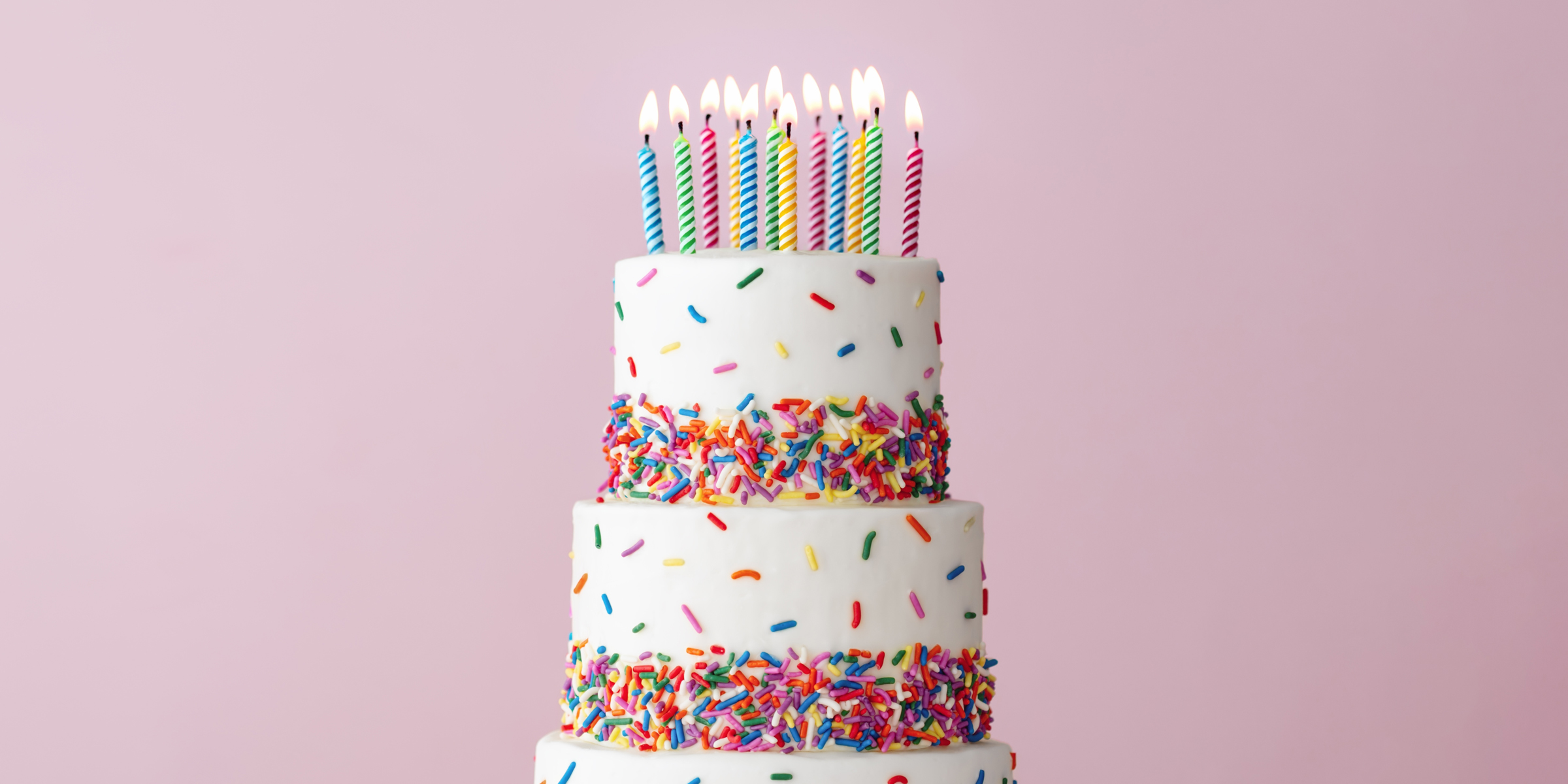 Pastel de cumpleaños de tres pisos con virutas de arco iris y velas encendidas | Fuente: Shutterstock