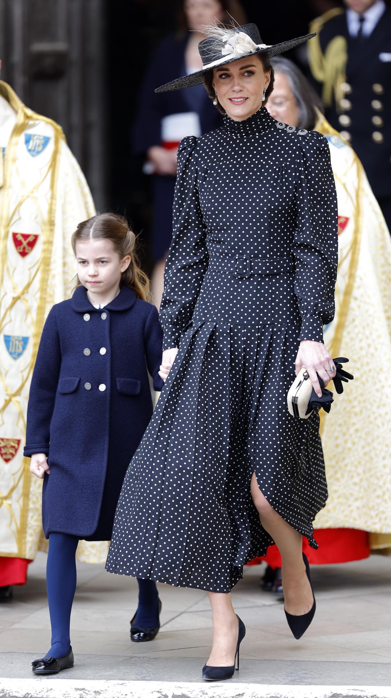 La princesa Charlotte camina de la mano de Catherine, duquesa de Cambridge, mientras salen de la Abadía de Westminster tras el servicio de acción de gracias por la vida del príncipe Felipe, duque de Edimburgo, el 29 de marzo de 2022, en Londres, Inglaterra. Charlotte lleva un abrigo azul marino abotonado sobre unas medias a juego y zapatos negros de charol, y va de la mano de Catherine, que luce un elegante vestido midi plisado de lunares blancos y negros, un sombrero de ala ancha con detalles florales y unos zapatos de tacón negros de punta. | Fuente: Getty Images