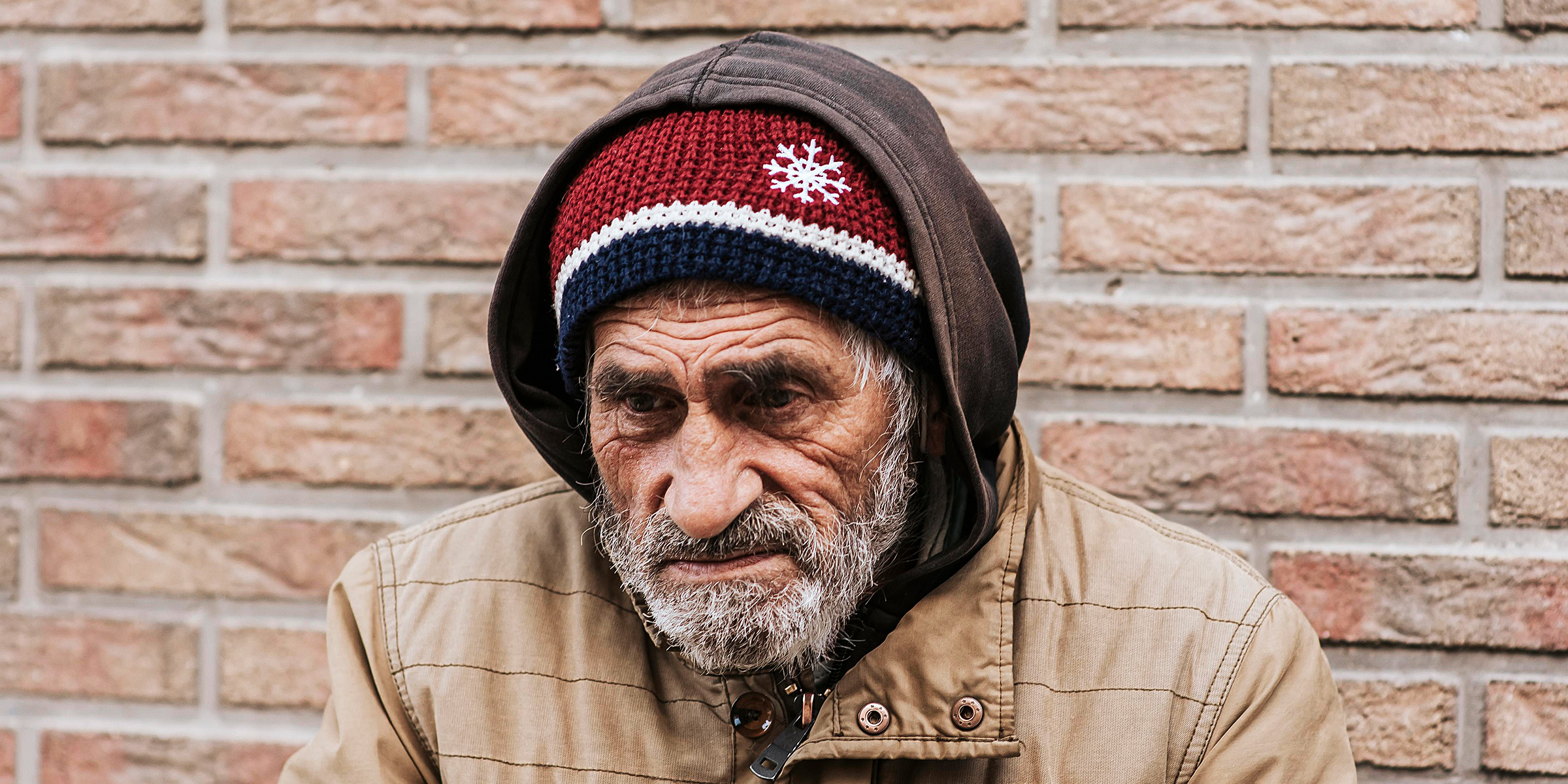 Un anciano de pie junto a un muro de ladrillos | Fuente: Freepik