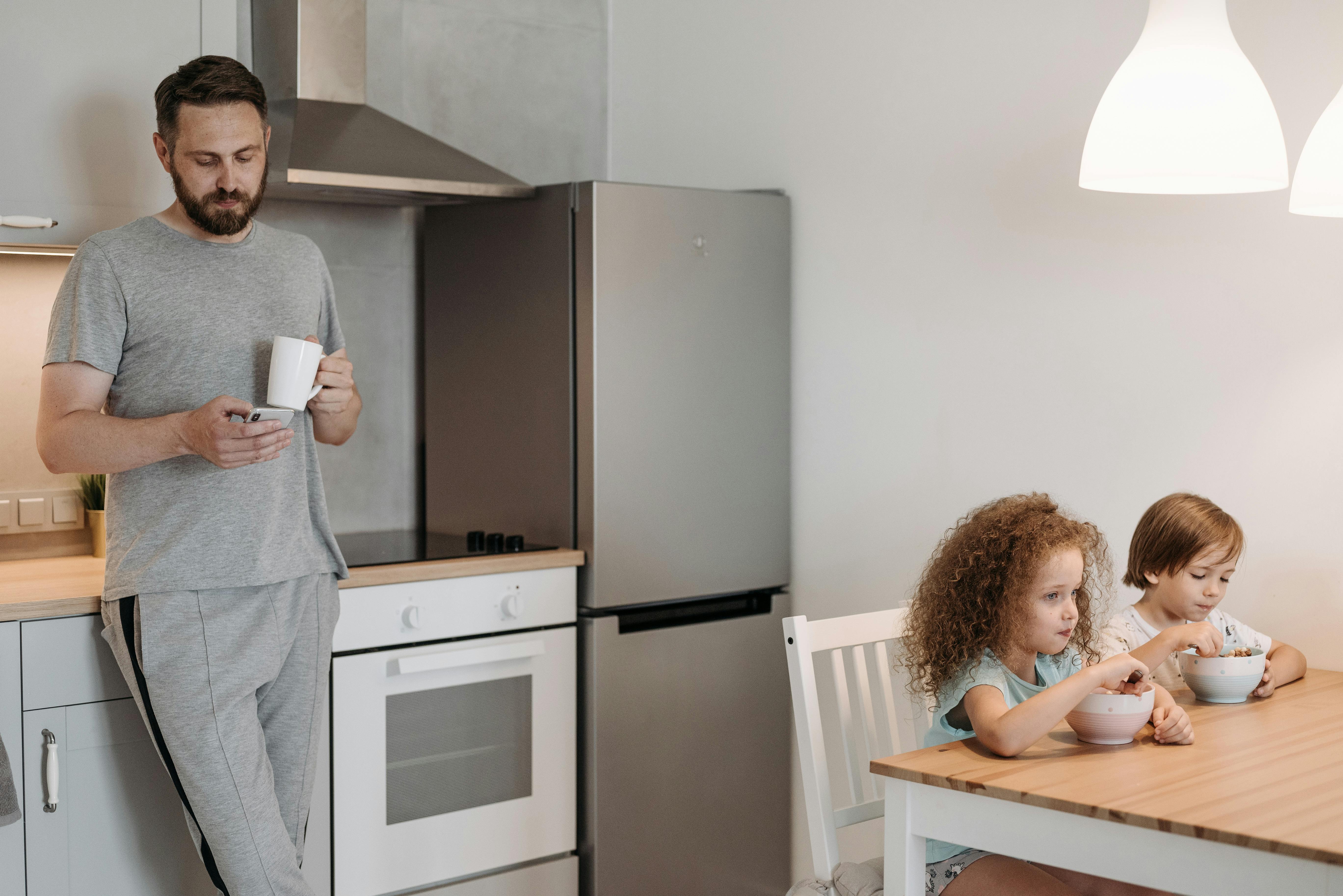 Un hombre usando su teléfono mientras sus hijos comen | Fuente: Pexels