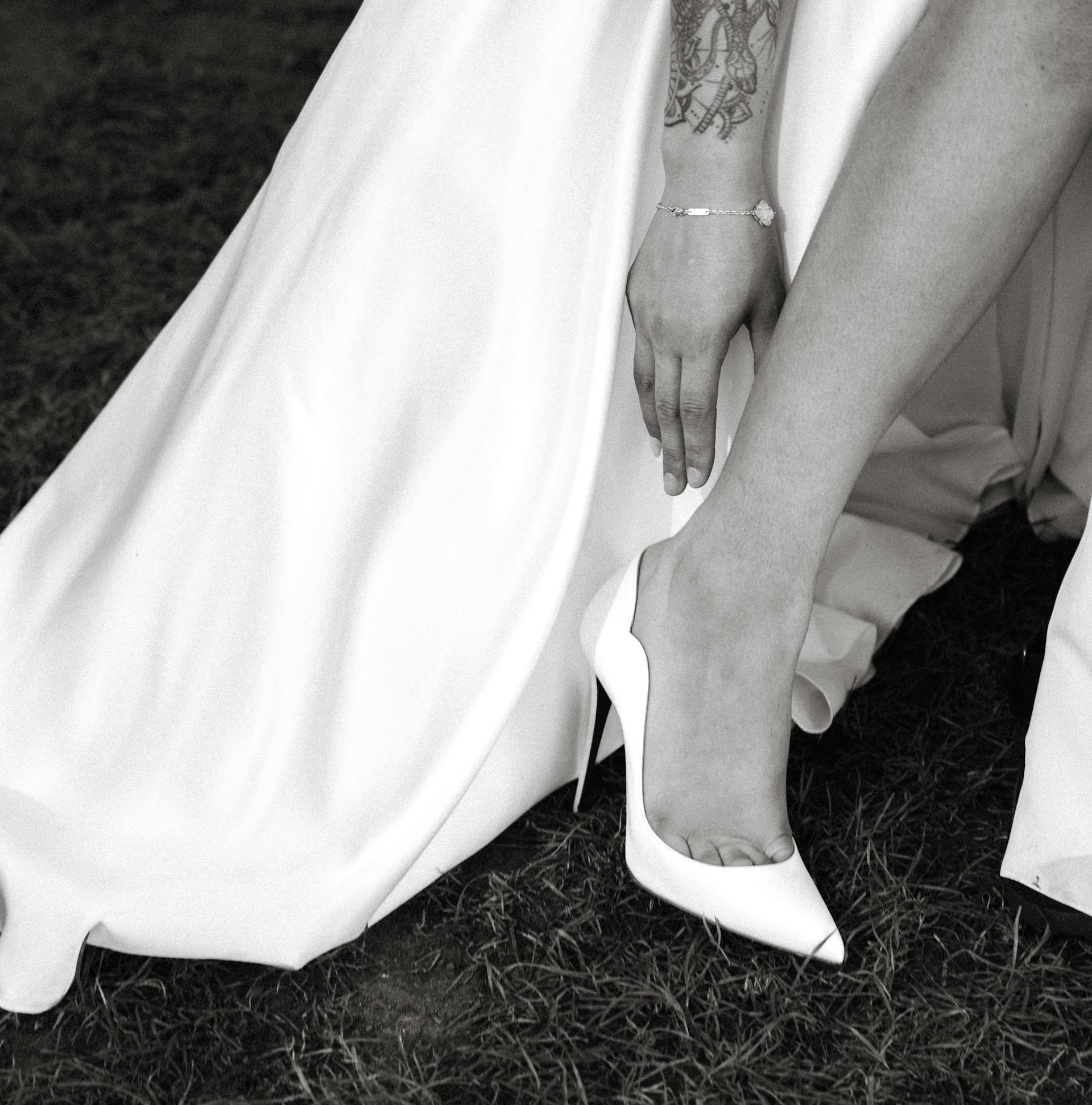 Primer plano de una novia alcanzando sus tacones mientras está de pie sobre la hierba | Fuente: Pexels