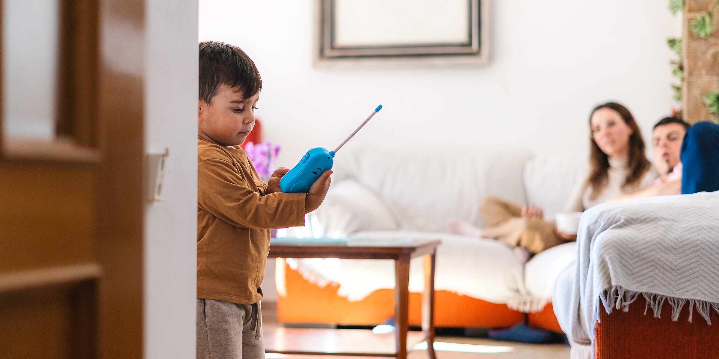 Un niño jugando con un walkie-talkie azul mientras dos adultos miran desde el sofá | Fuente: Shutterstock