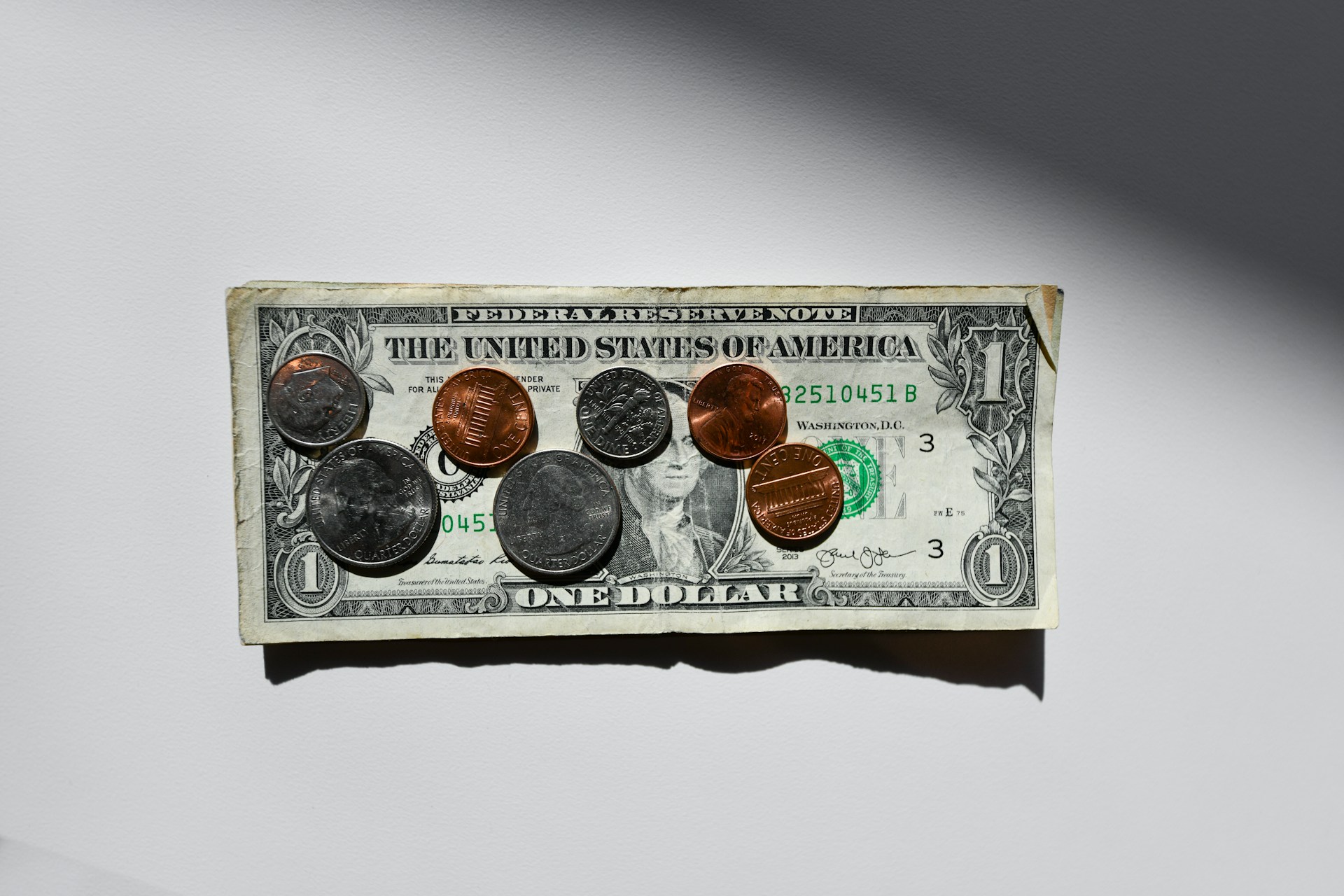 Monedas sobre una fina pila de billetes de dólar | Fuente: Unsplash