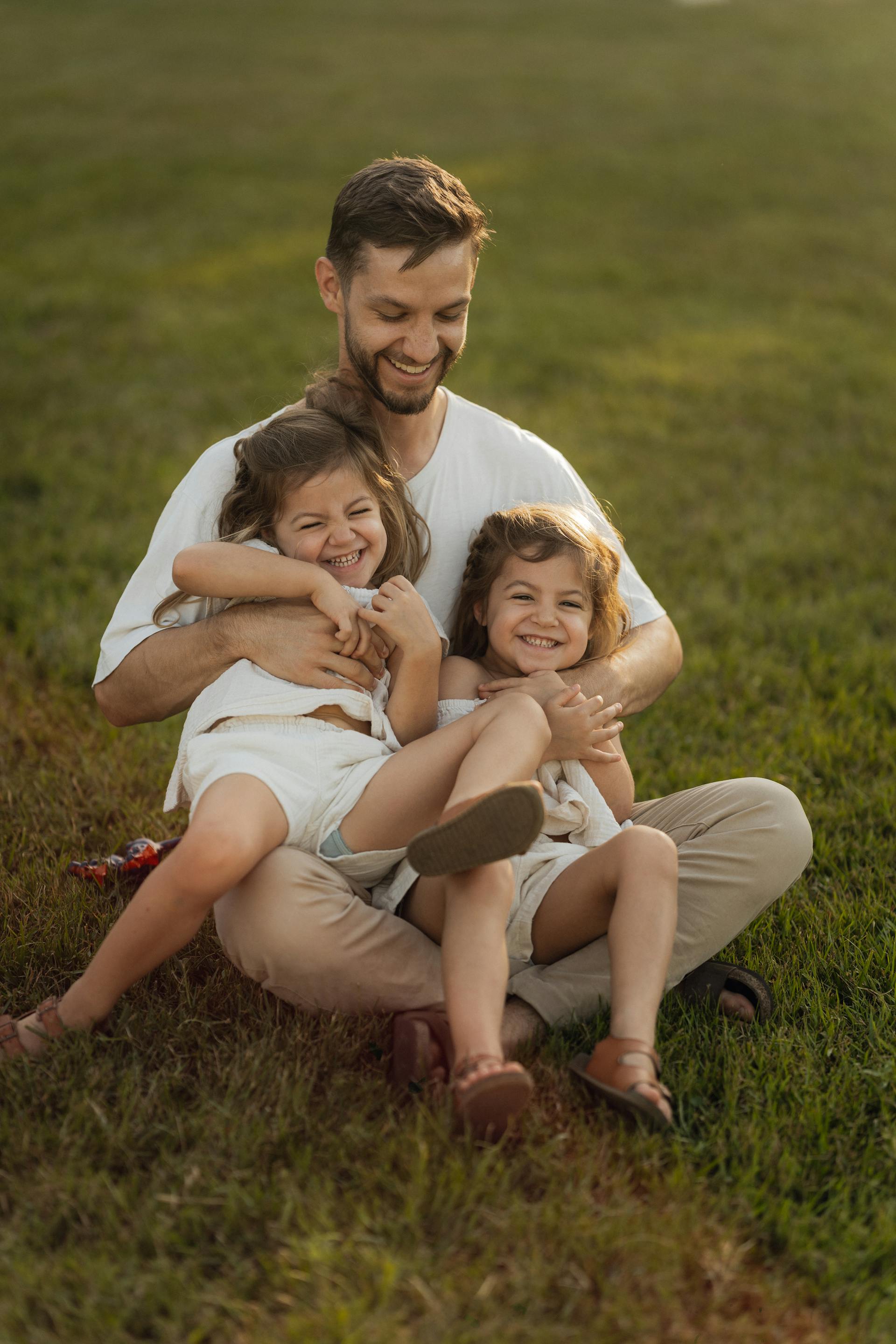 Un padre jugando con sus hijas en el césped | Fuente: Pexels