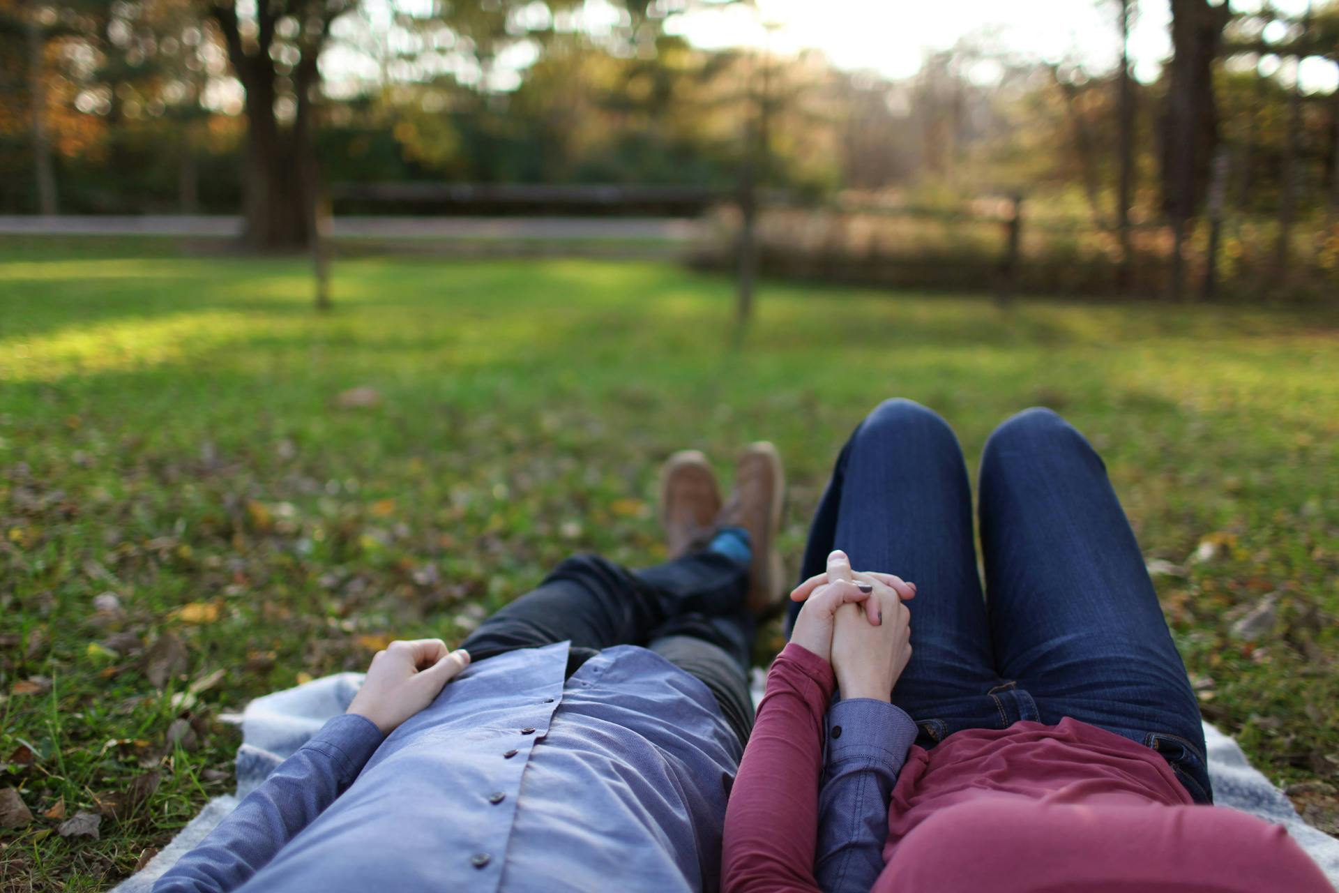 Una pareja acostada en la hierba tomada de la mano | Fuente: Pexels