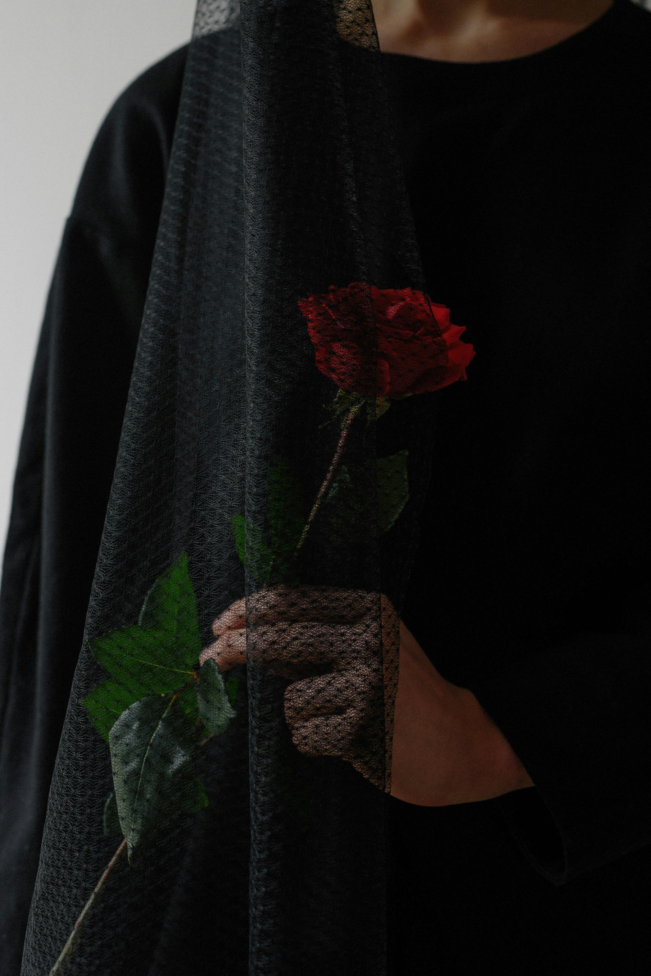 Una mujer vestida de negro sosteniendo una rosa roja | Fuente: Pexels
