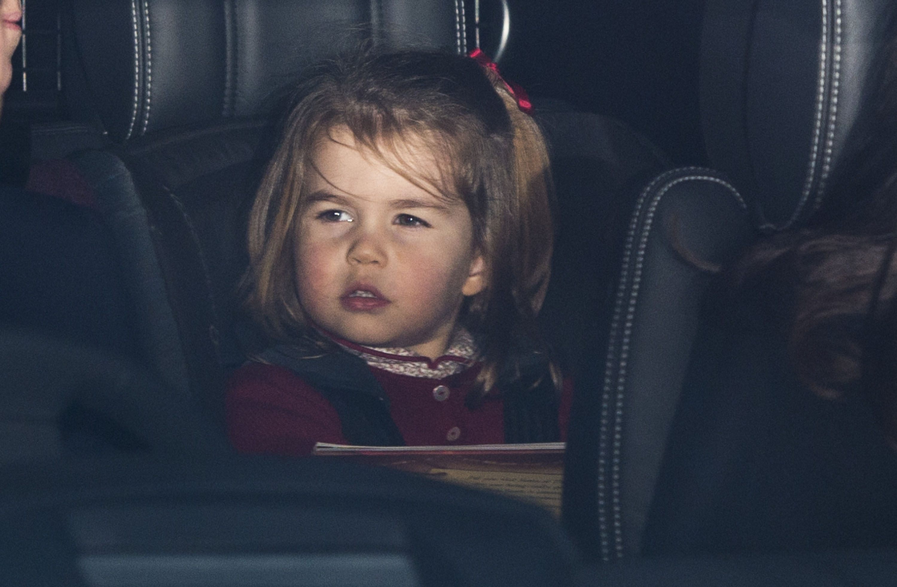 La princesa Charlotte de Cambridge asoma la cabeza desde el asiento trasero de un automóvil al llegar a la comida navideña anual de la familia real al completo en el Palacio de Buckingham, el 20 de diciembre de 2017, en Londres, Inglaterra. La pequeña princesa lleva un festivo cárdigan burdeos sobre un top estampado con cuello, y el pelo peinado con un lazo rojo a juego. | Fuente: Getty Images