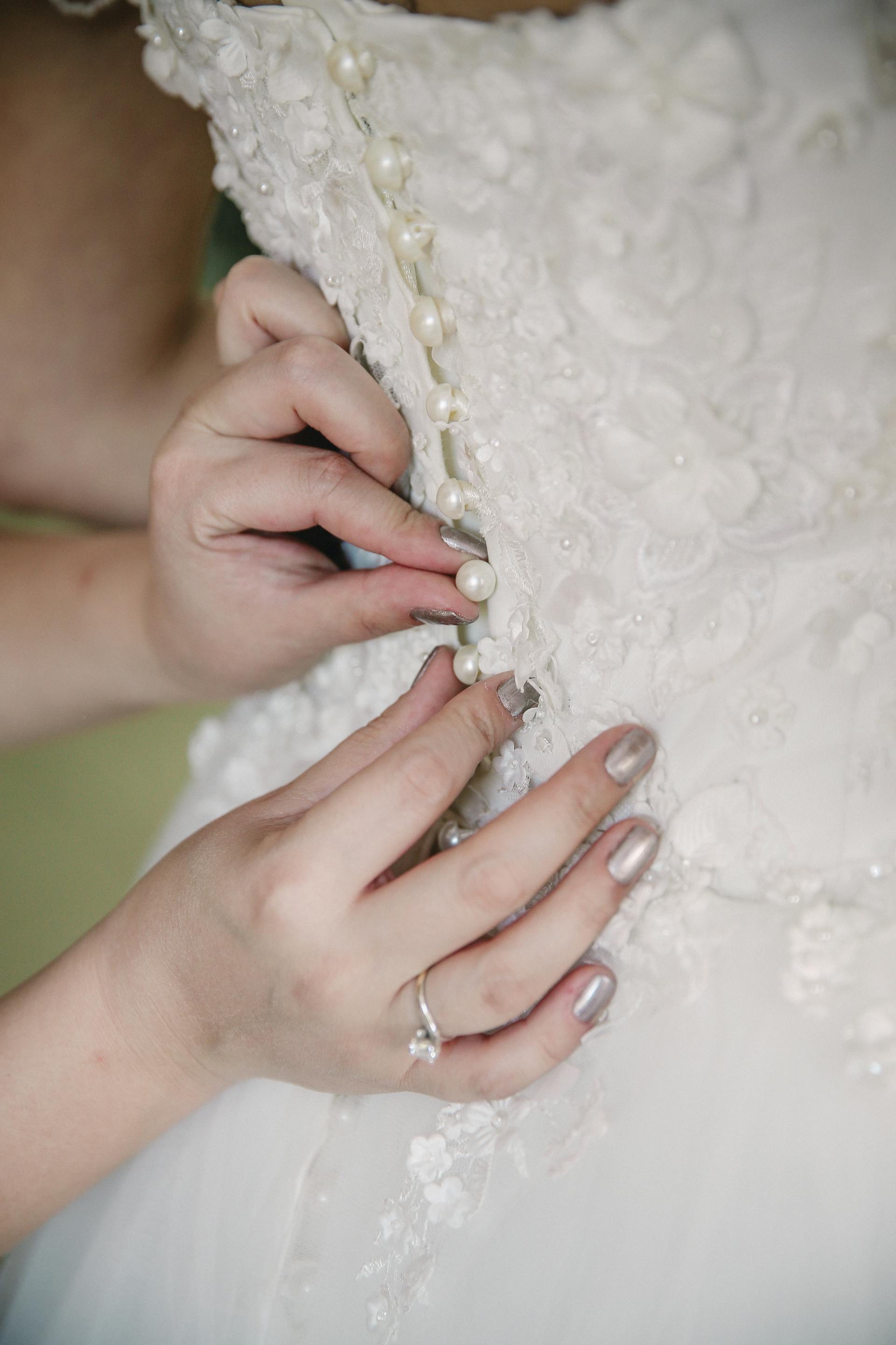 Manos abotonando un vestido de novia | Fuente: Pexels