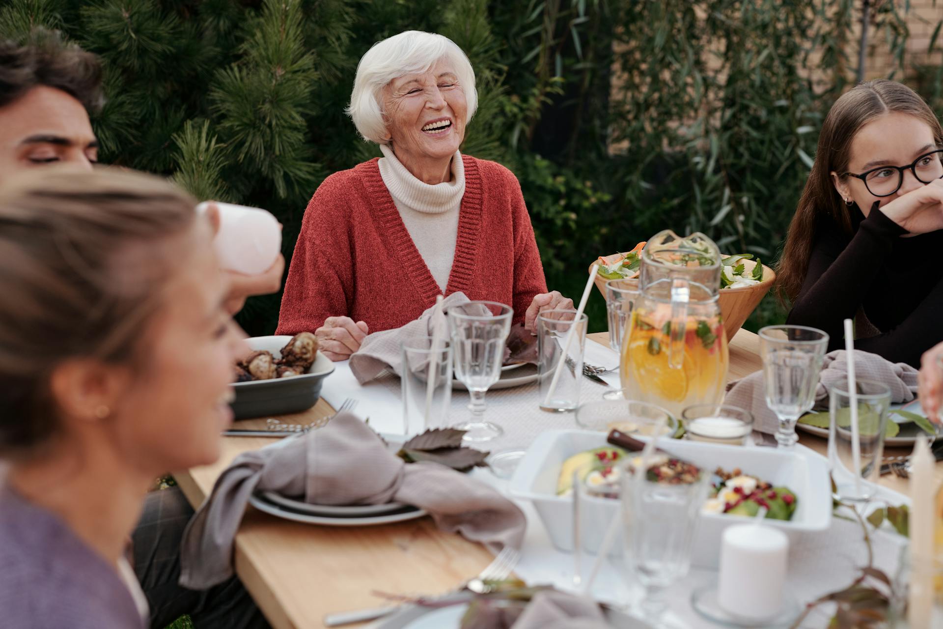Una mujer mayor se ríe mientras cena con su familia en el patio trasero | Fuente: Pexels