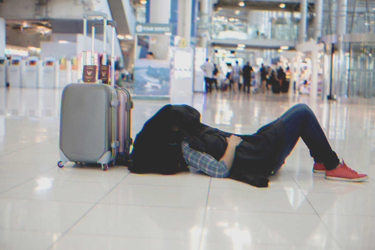 Hombre tumbado en el suelo de un aeropuerto | Fuente: Shutterstock