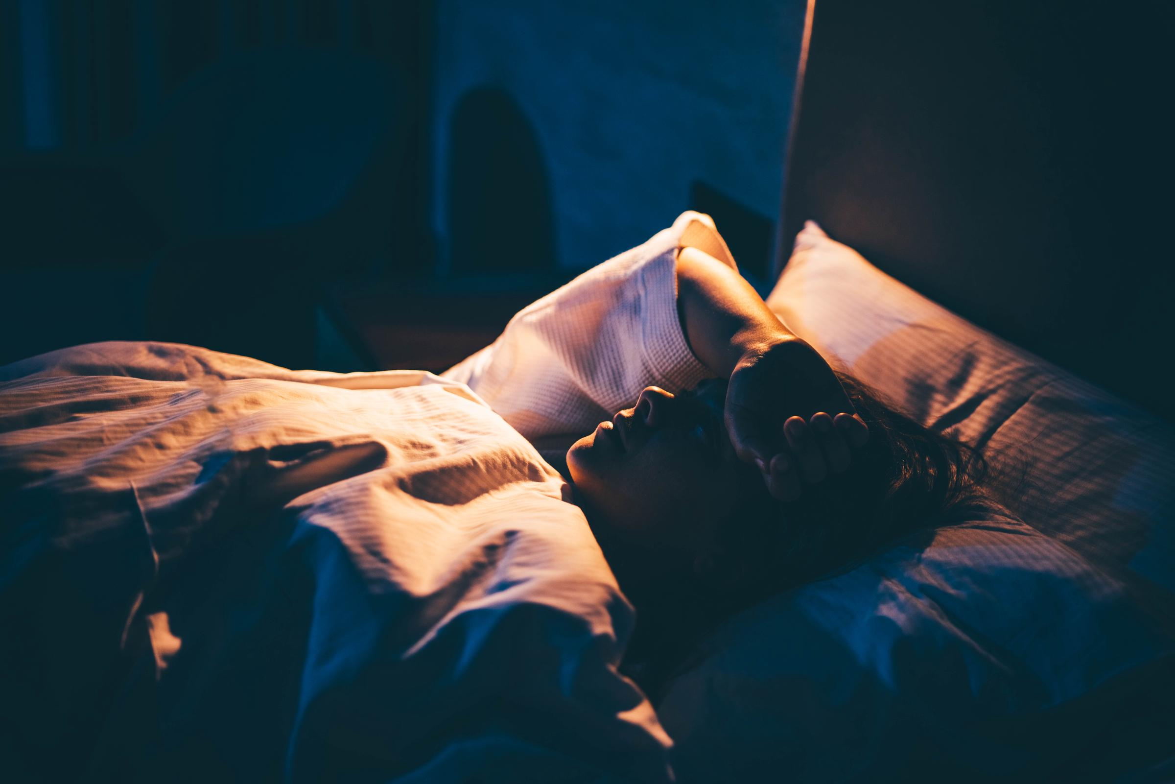 Mujer joven que lucha contra el insomnio, tumbada en la cama con la mano en la frente | Fuente: Getty Images