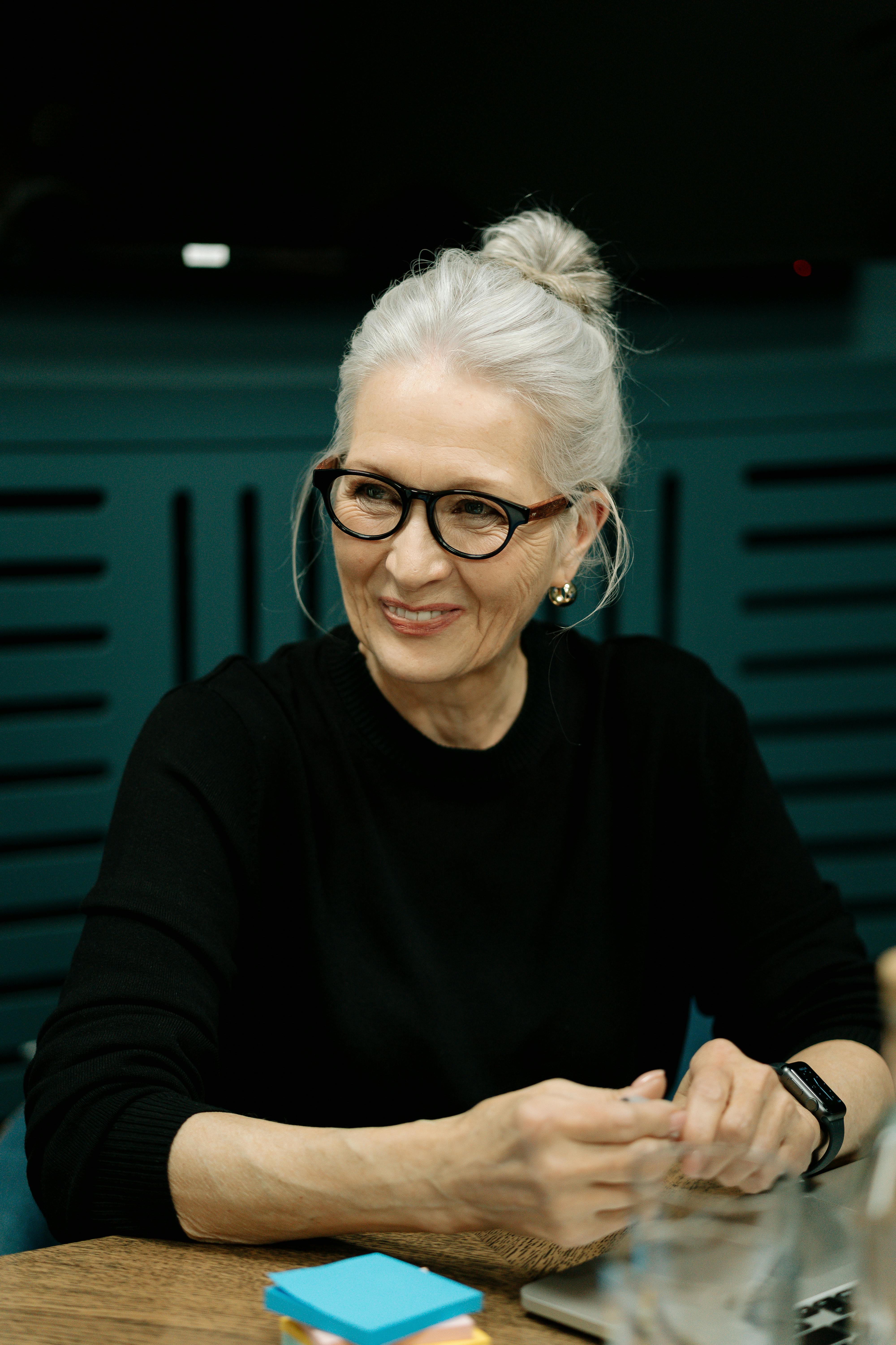 Una mujer mayor sonriente sentada a una mesa | Fuente: Pexels