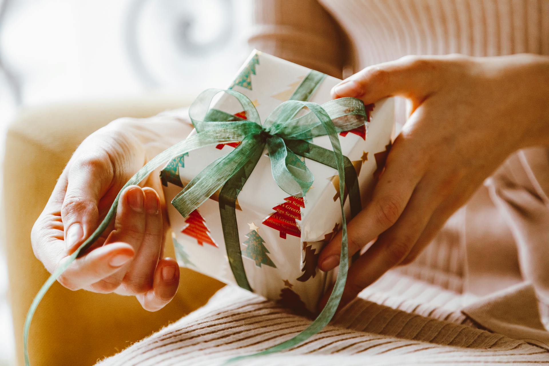 Primer plano de las manos de una mujer a punto de desenvolver un regalo de Navidad | Fuente: Pexels