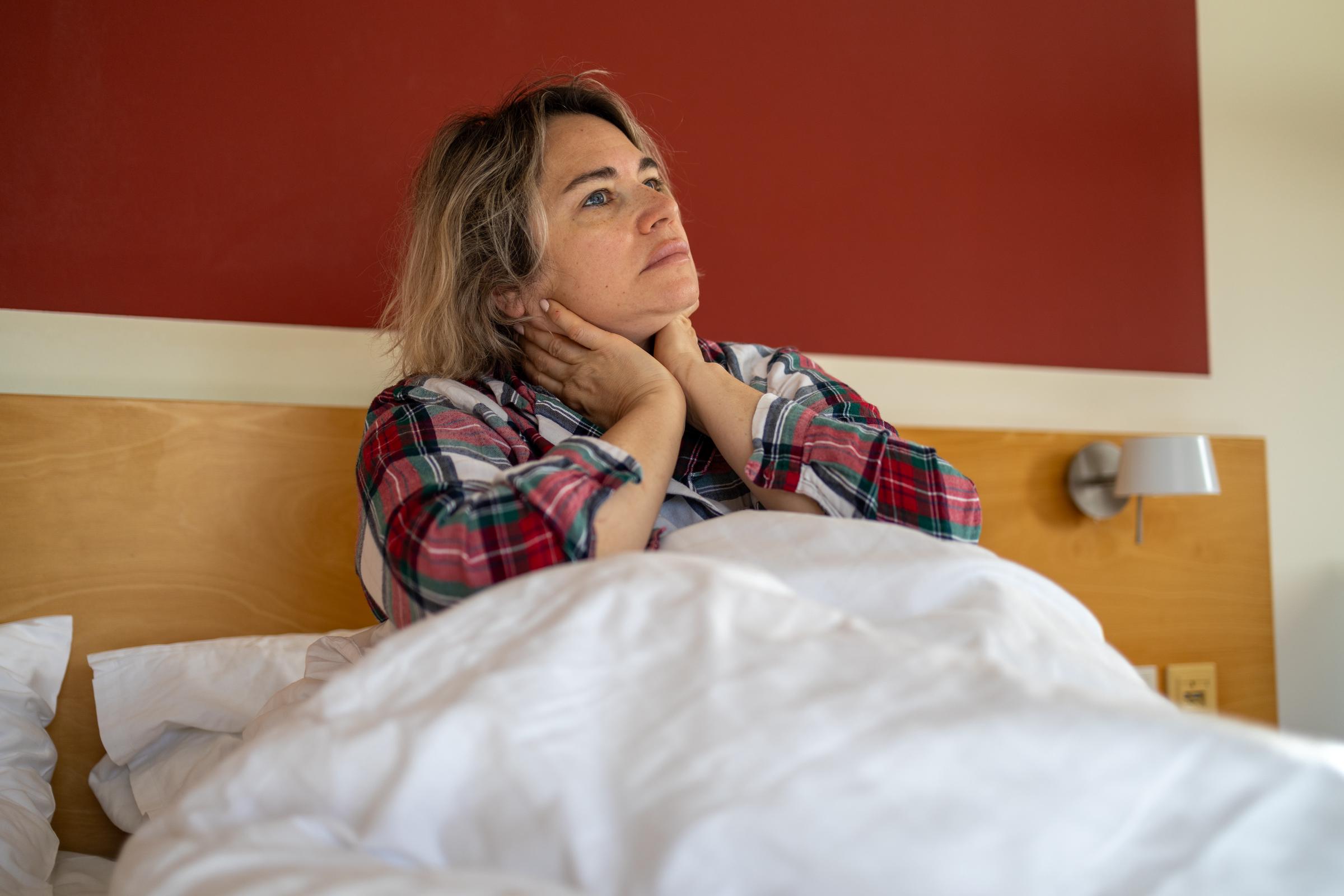 Mujer cansada sentada en la cama, sujetándose el cuello con dolor, simbolizando el estrés, el agotamiento y las luchas por la salud mental | Fuente: Getty Images