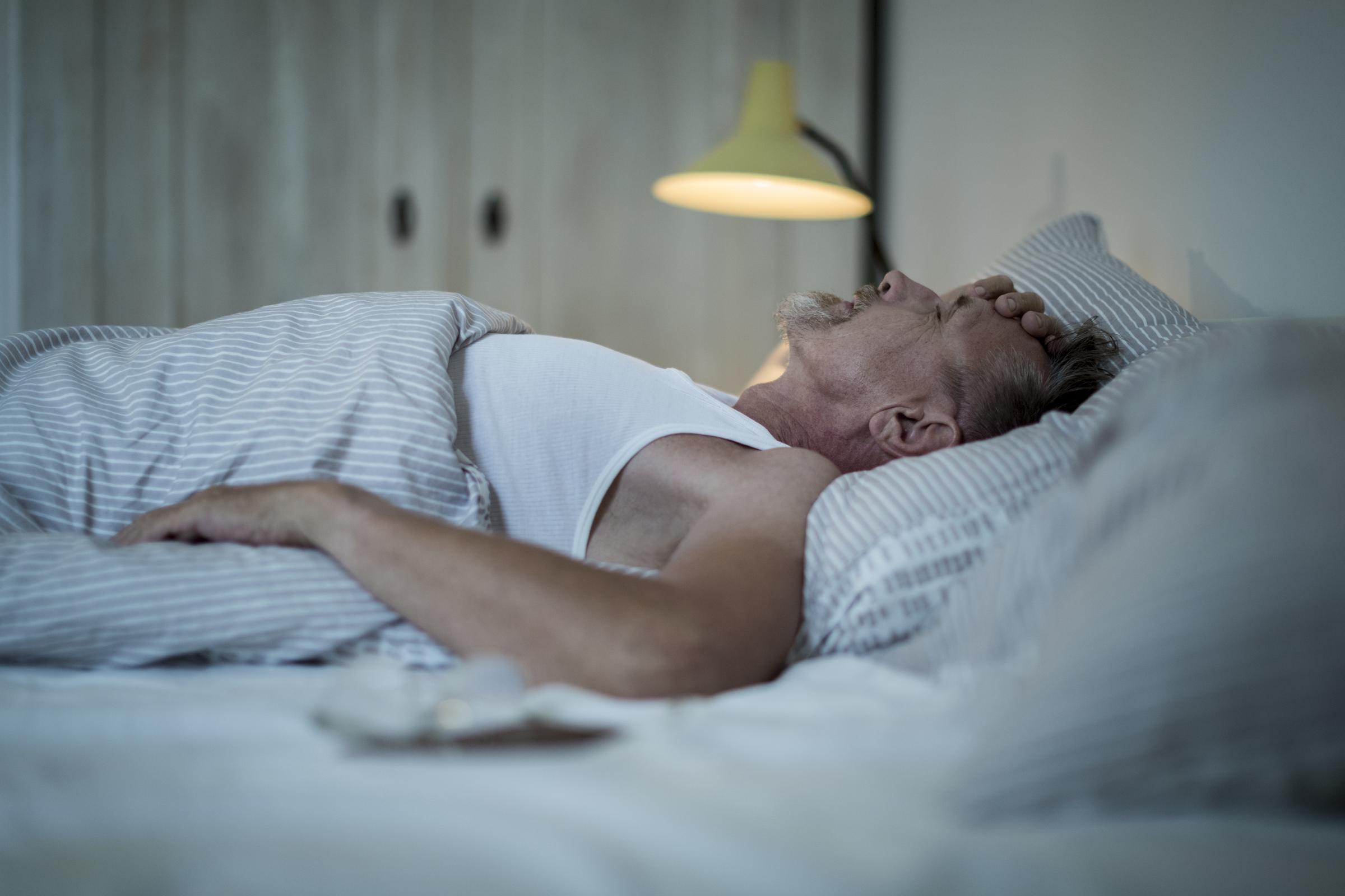 Hombre tumbado en la cama por la noche, sintiéndose indispuesto y sin poder dormir | Fuente: Getty Images