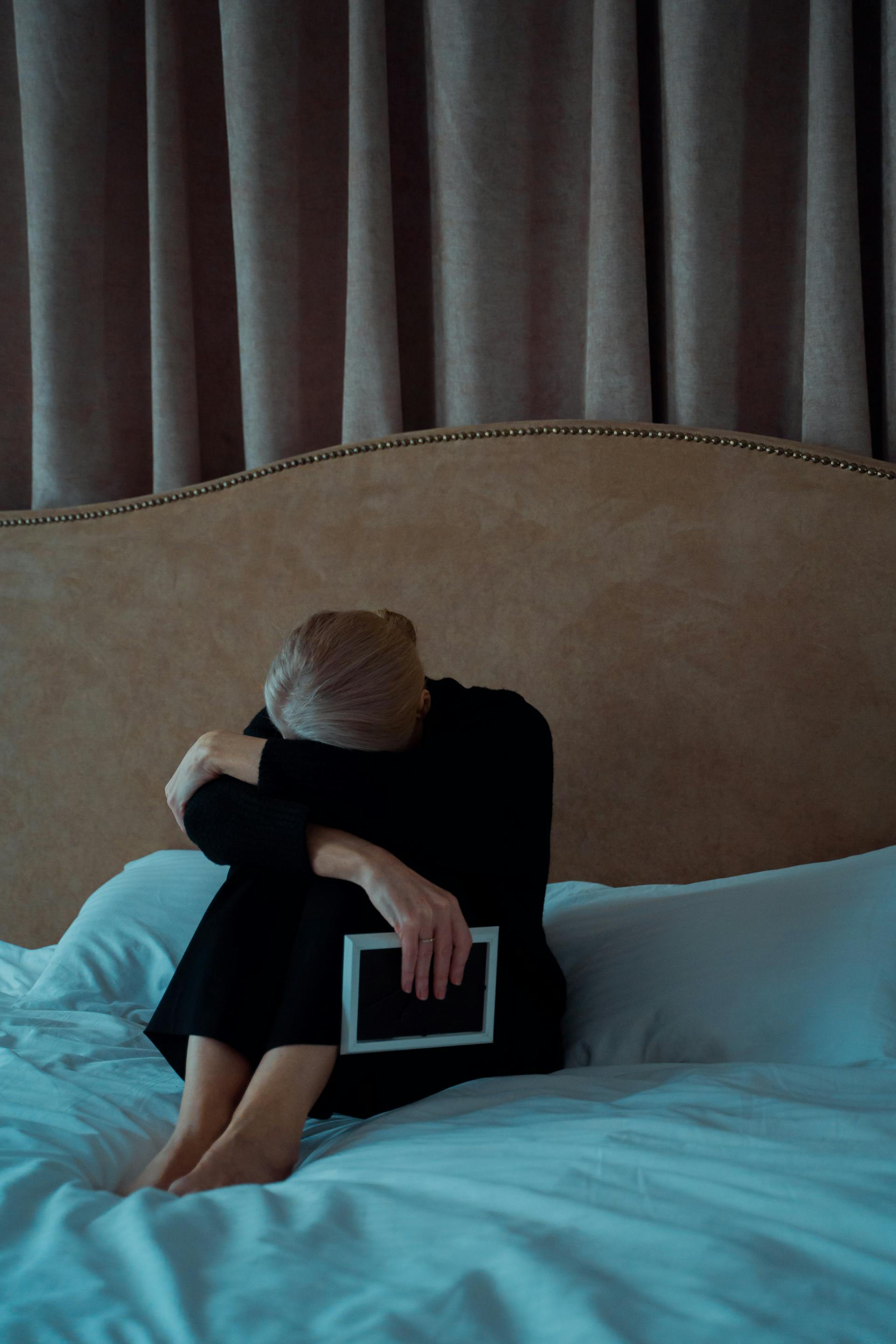 Una anciana triste sostiene un marco de fotos sentada en su cama | Fuente: Pexels