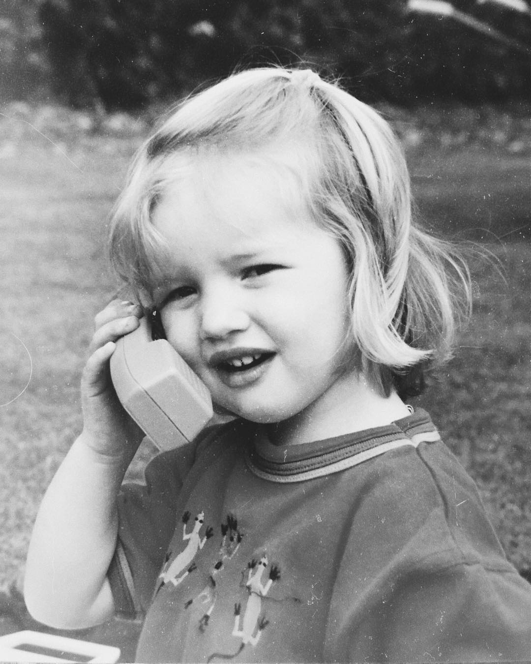 Rosie Alice Huntington-Whiteley de niña, sujetando un teléfono de juguete al aire libre en una encantadora instantánea en blanco y negro. | Fuente: Instagram/rosiehw