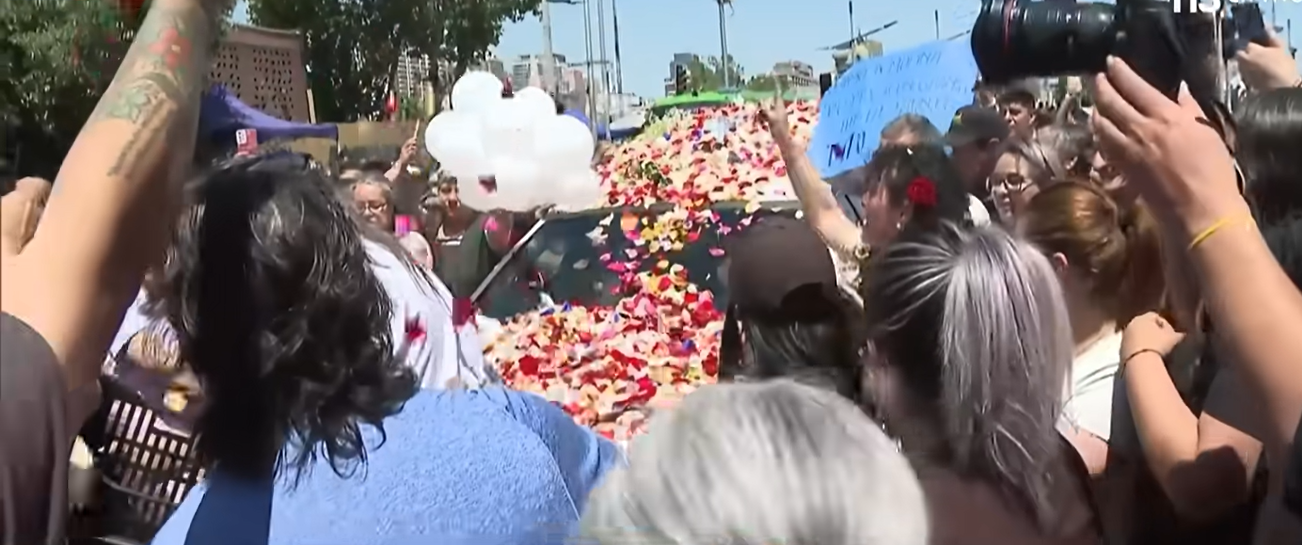 Personas lanzando pétalos de flores a la carroza fúnebre donde transportaban al fallecido actor Héctor Noguera | Fuente: YouTube/Teletrece