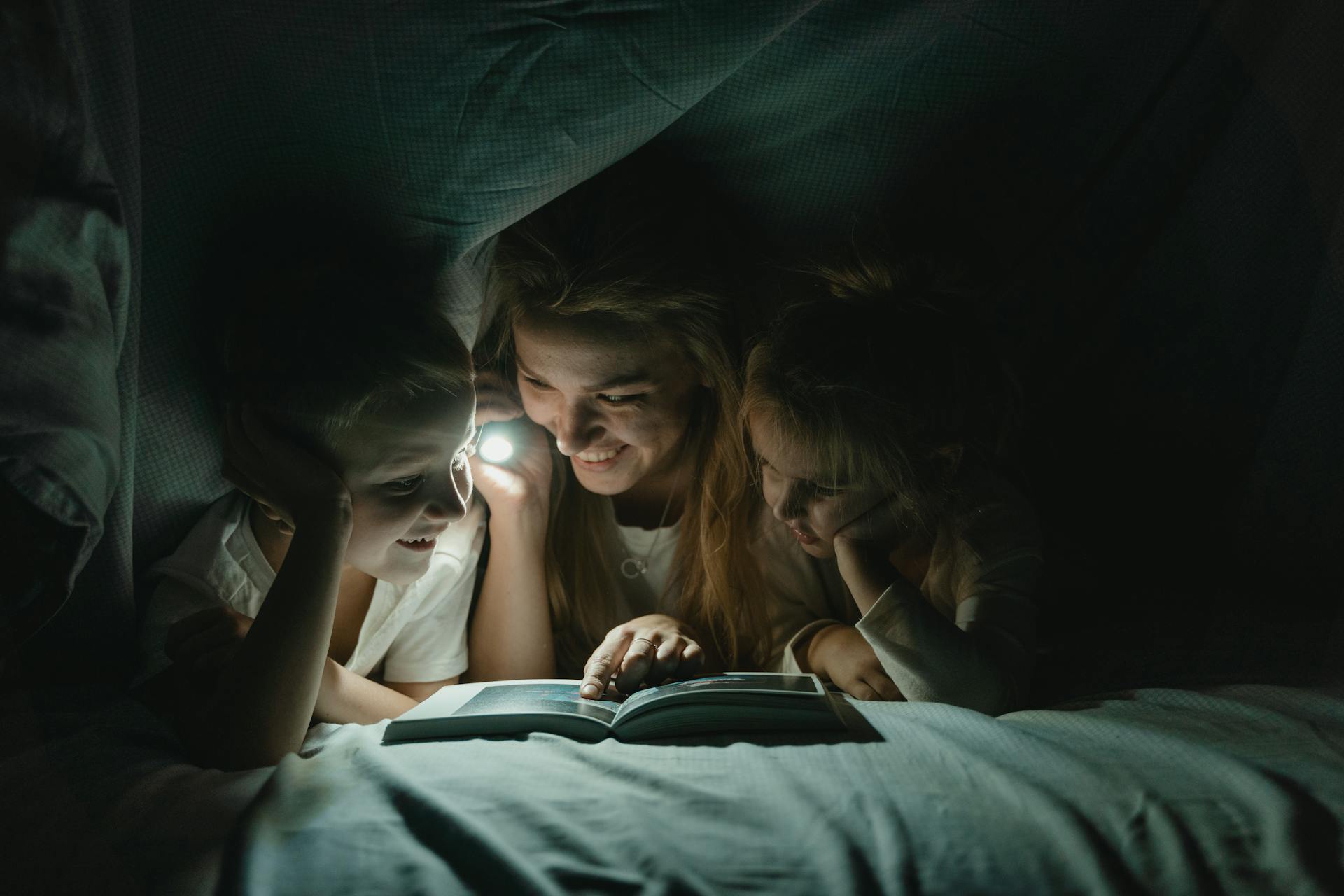 Una mujer sostiene una linterna y lee un cuento a sus hijos | Fuente: Pexels