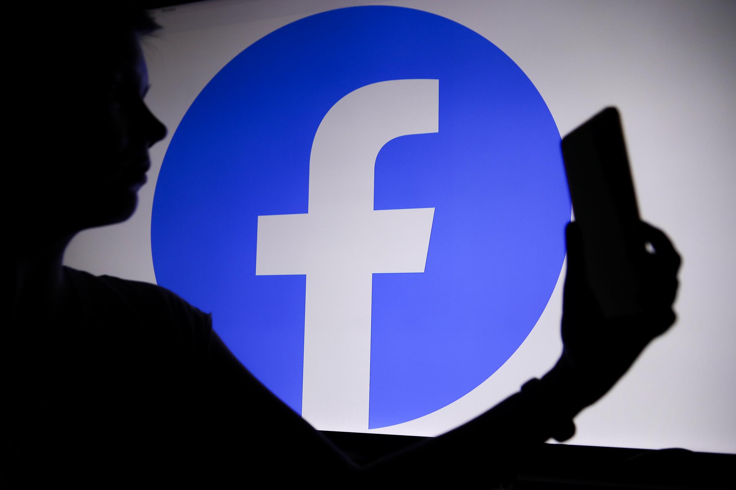 El logotipo de Facebook con una persona sosteniendo un teléfono en la mano. | Fuente: Getty Images