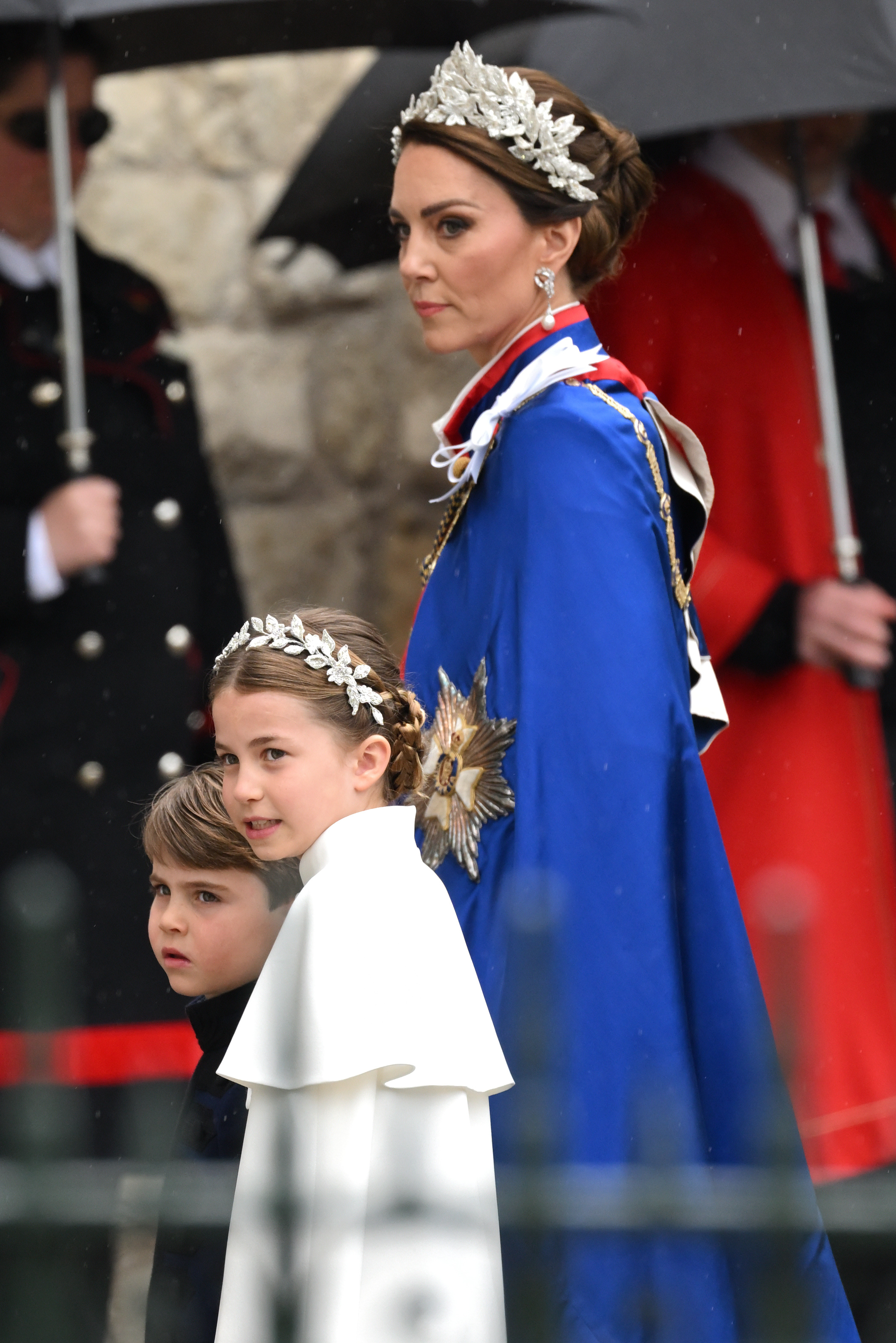 La princesa Charlotte llega junto al príncipe Louis y a Catherine, princesa de Gales, a la Abadía de Westminster para la coronación del rey Carlos III y la reina Camilla el 6 de mayo de 2023, en Londres, Inglaterra. Charlotte luce un vestido de Alexander McQueen en color marfil con una capelina y un elaborado tocado de flores de cristal y hilos de plata, muy a la manera de su madre, mientras camina junto al príncipe Louis, que lleva una túnica azul marino de Dege & Skinner; por su parte, Catherine luce majestuosa con el manto de la Real Orden Victoriana y un tocado floral a juego. | Fuente: Getty Images