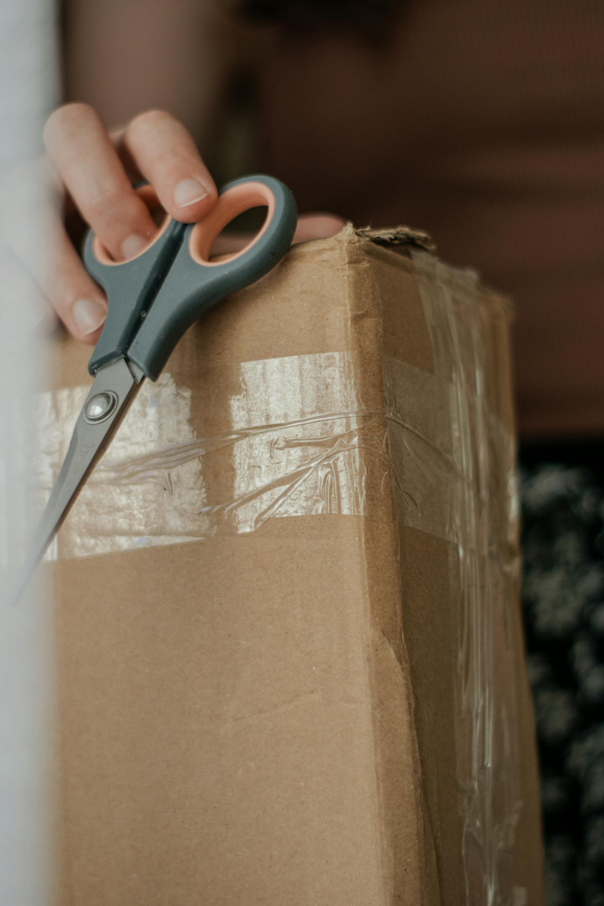 Primer plano de una mujer sujetando una caja de cartón y unas tijeras | Fuente: Pexels