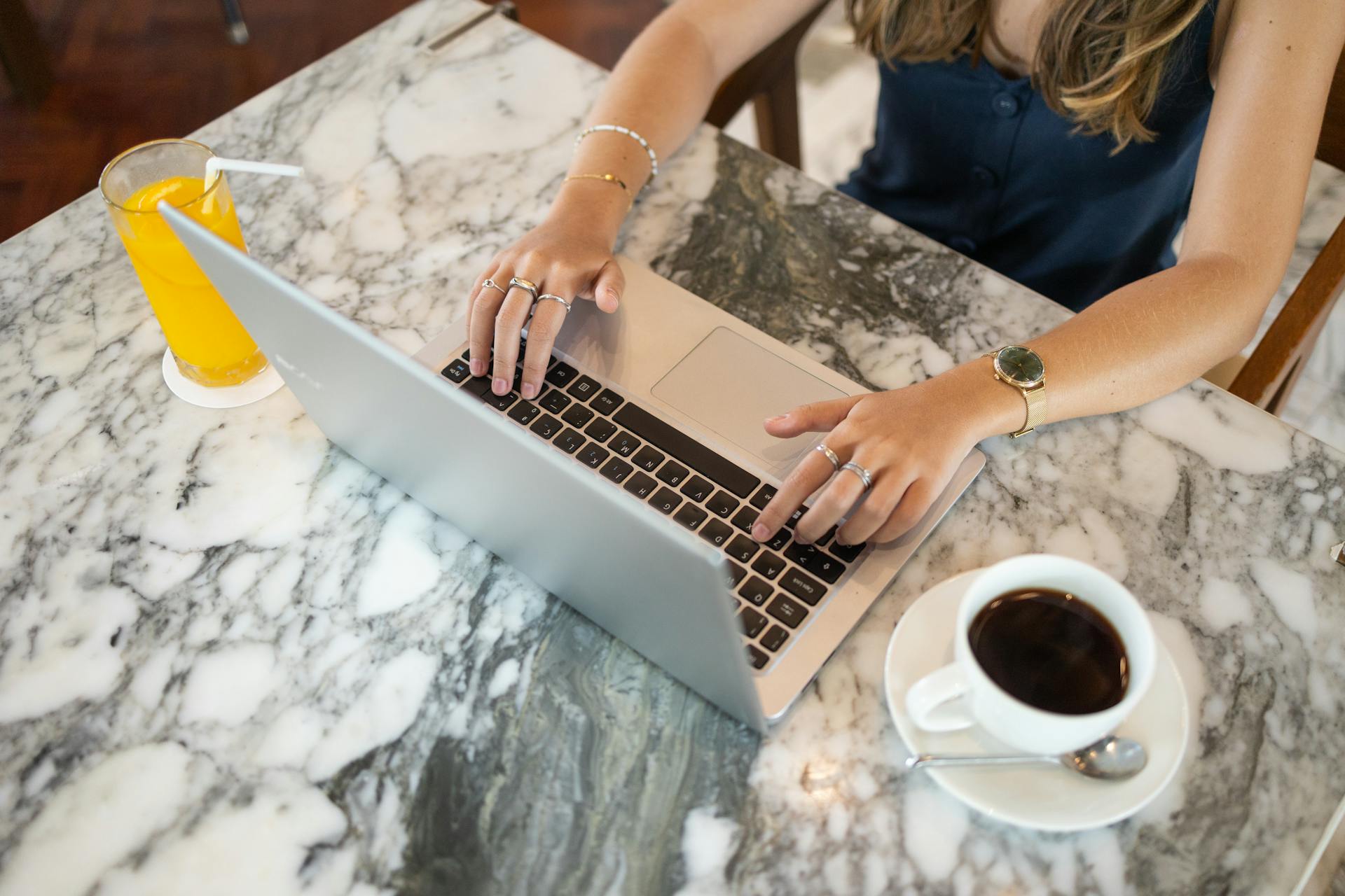 Una mujer trabajando en su portátil con una taza de café y zumo sobre la mesa delante de ella | Fuente: Pexels