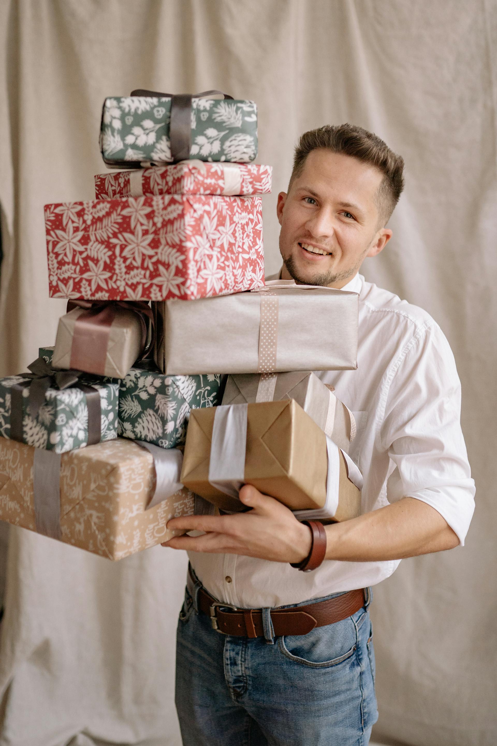 Un hombre con camisa blanca y vaqueros sujetando una gran pila de regalos envueltos | Fuente: Pexels