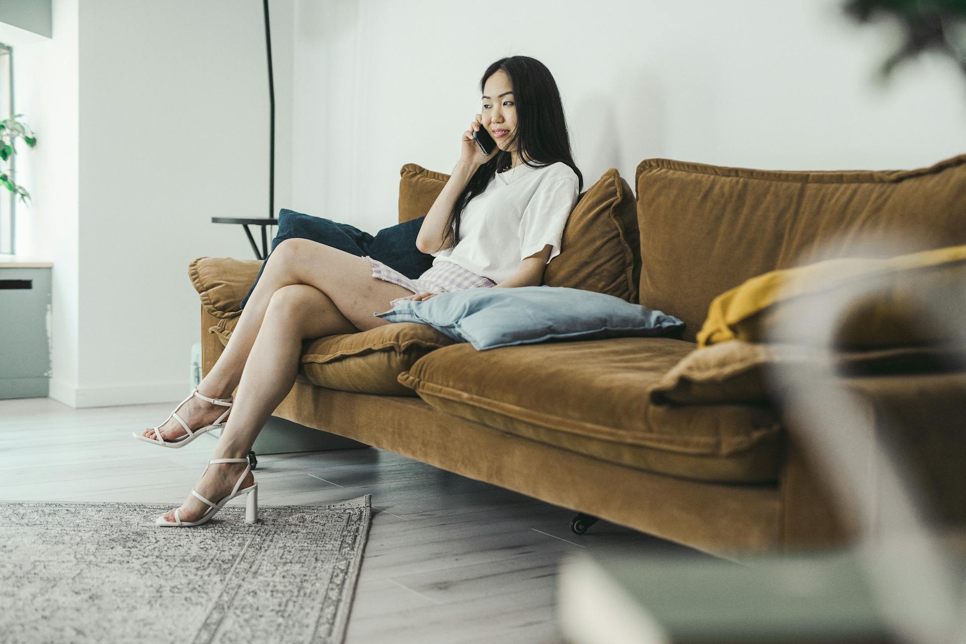 Una mujer joven con tacones altos sentada en un sofá marrón hablando por teléfono | Fuente: Pexels