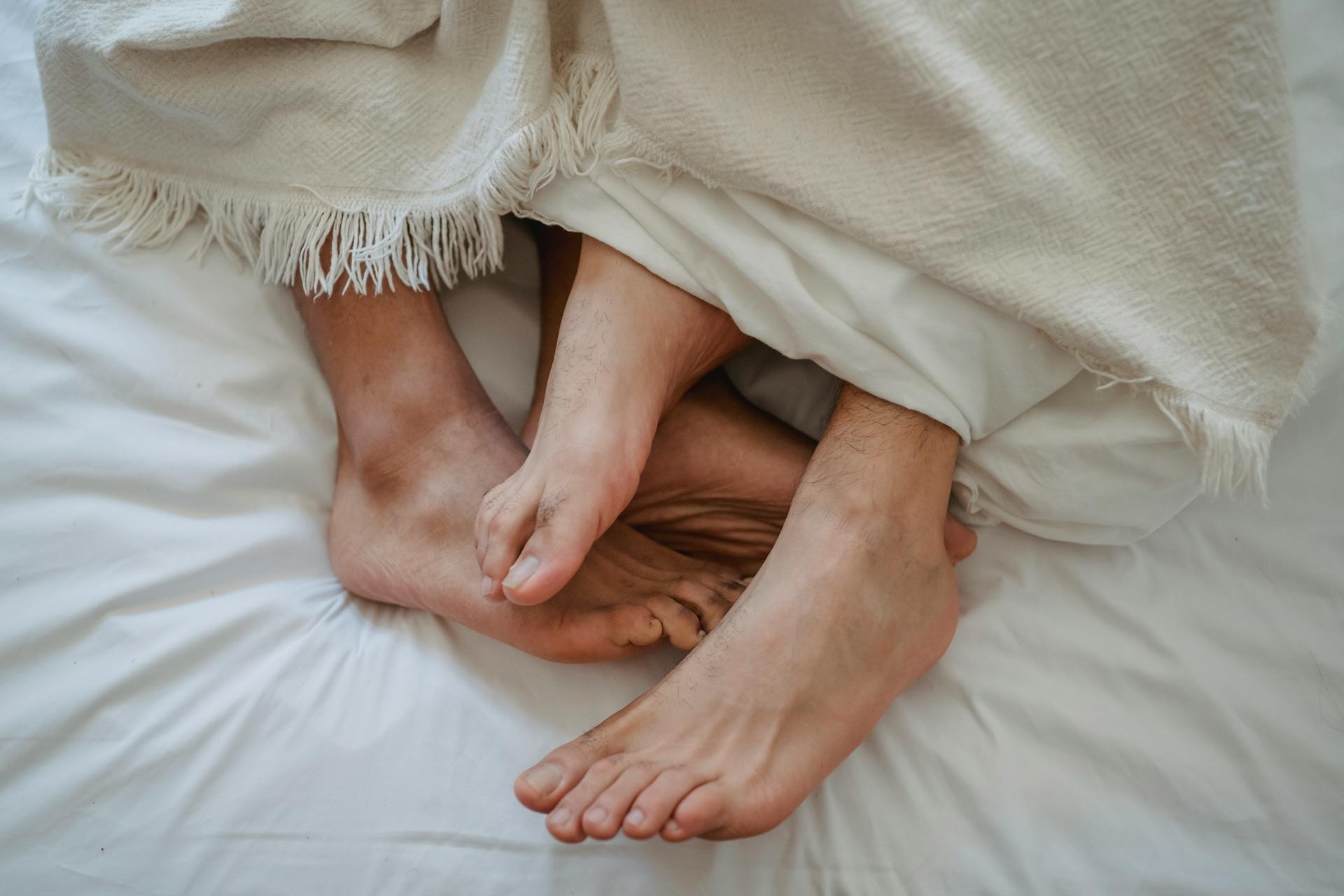 Pies de dos hombres entrelazados en la cama | Fuente: Pexels